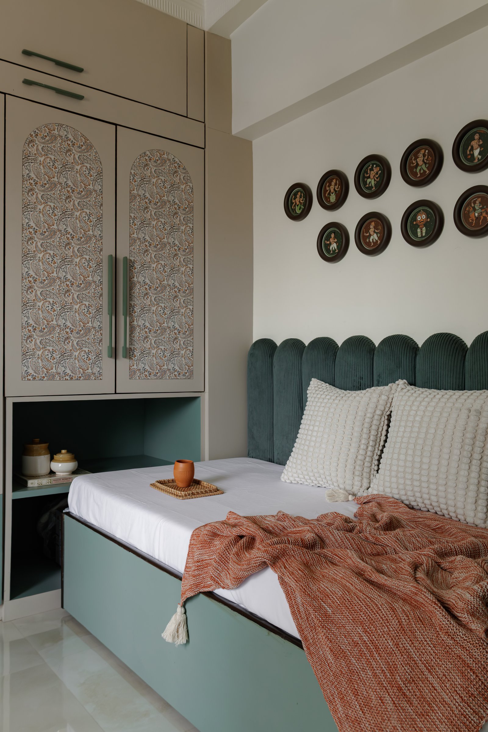 The guest bedroom, where a grid of Dashavatar paintings in the Konkan Ganjifa tradition presides over a sage and terracotta palette