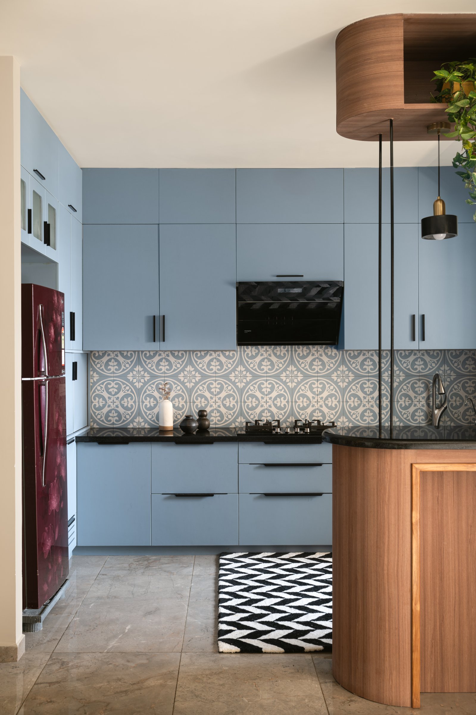 The kitchen seen at close range: the curved wooden counter, the patterned cement-tile backsplash, and a deep maroon refrigerator at the far end