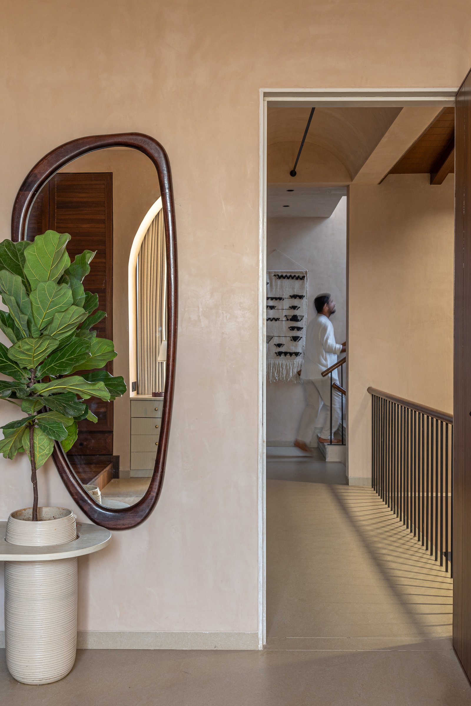An organic-edged dark wood mirror frames the passage, the resident mid-stride within it