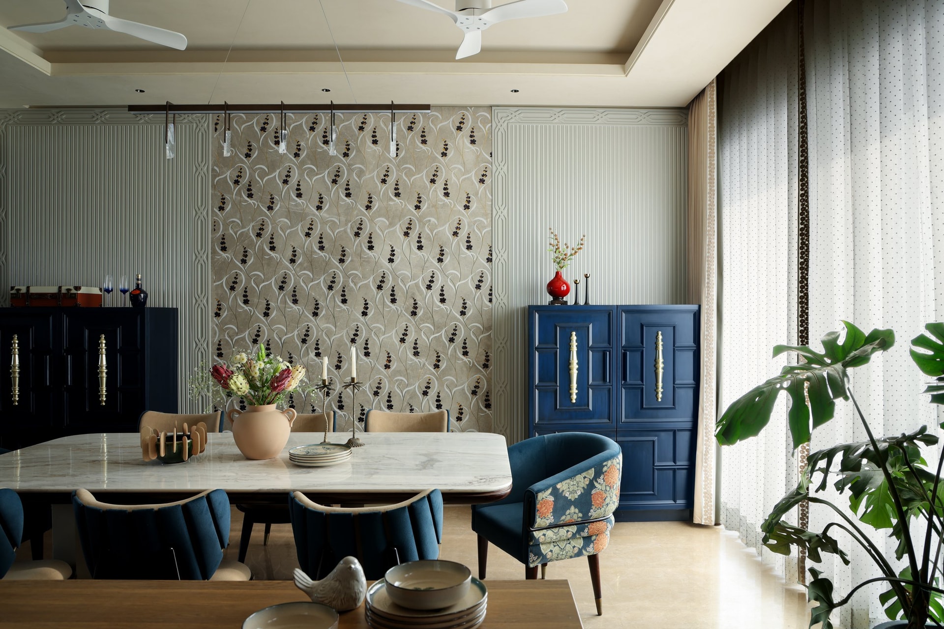 The dining room, anchored by a cobalt cabinet with ornate ivory handles and a patterned wall of trailing botanical motifs