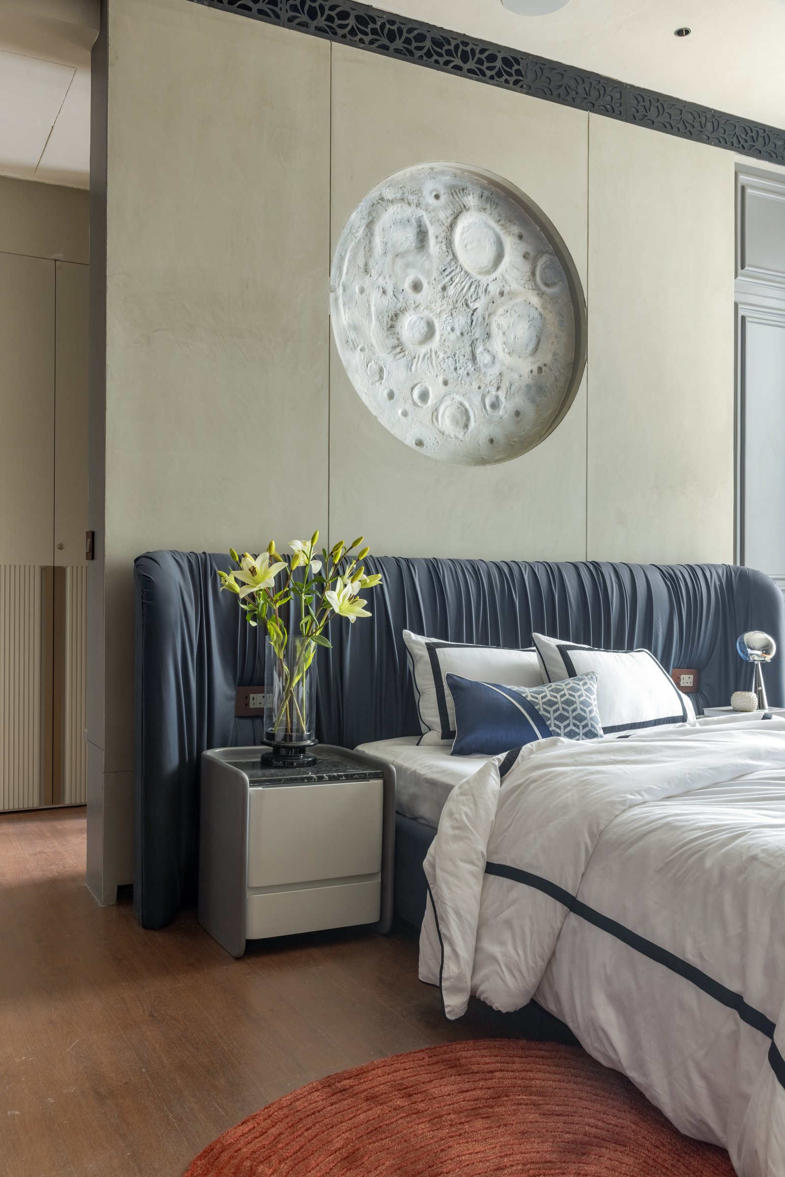 The second bedroom, where a gathered navy headboard runs beneath a sculpted lunar relief on pale plaster