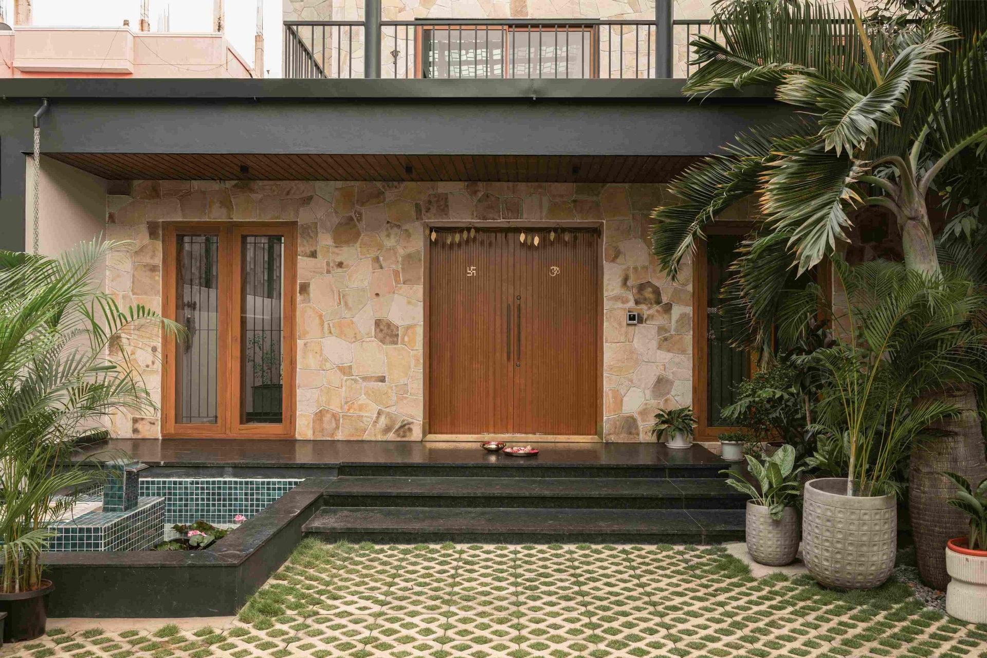 The entry portico, where a lotus pond and grass-laid paver grid soften the threshold into the home