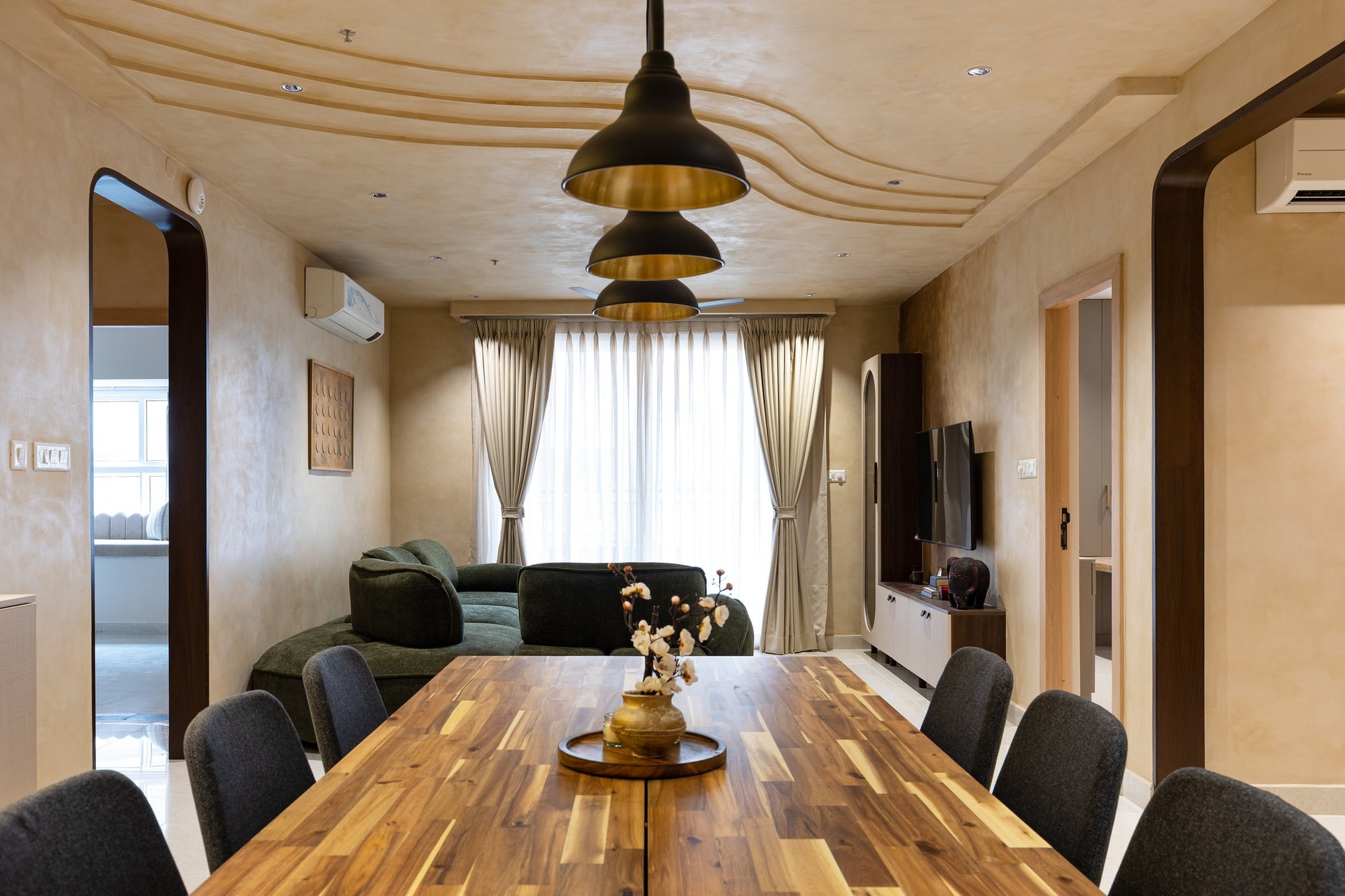 Looking from the dining end toward the balcony, three industrial pendants with brass-toned interiors anchor the long table