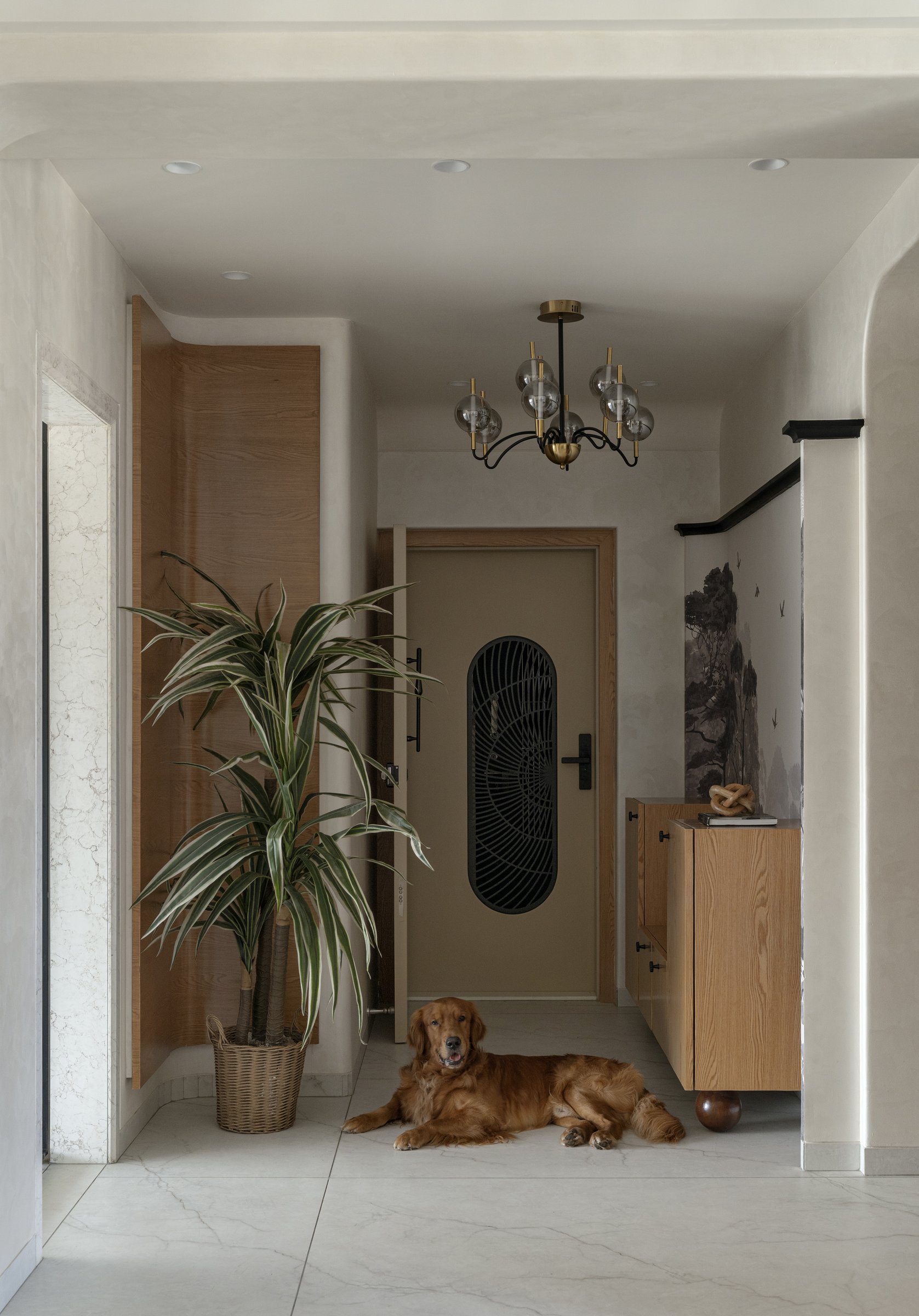 The foyer: a monochromatic mural, a brass-and-glass chandelier, and a wood console set the home's emotional register before the rooms truly begin