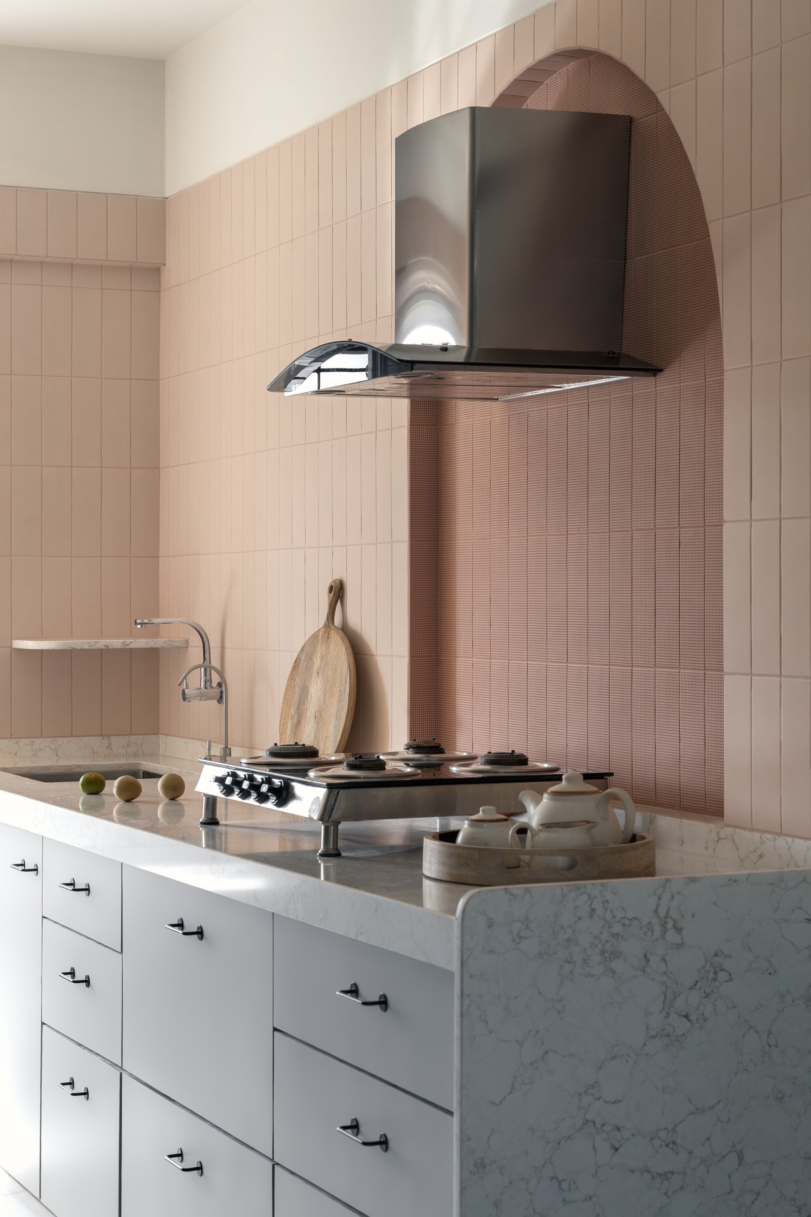 The kitchen's blush-toned tiles and arched niche behind the chimney turn a functional space into a small chapel of domestic ritual