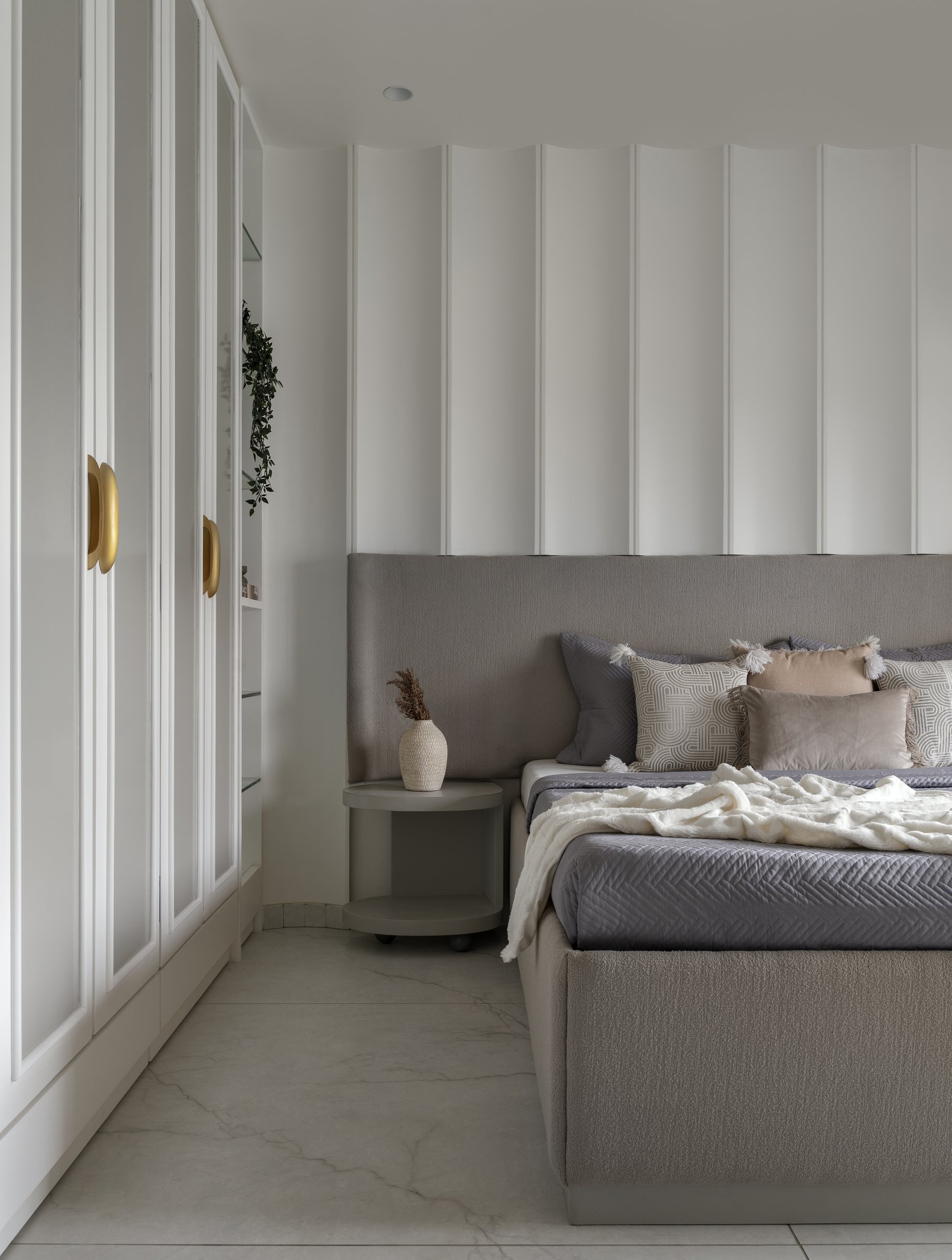 The second bedroom takes a cooler register: a soft grey upholstered headboard meets a wall of vertical fluted panelling