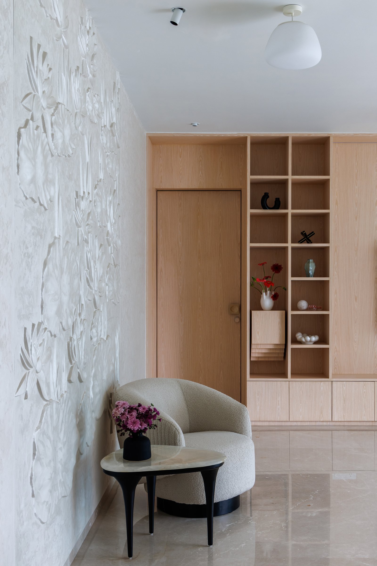 A quiet vestibule near the bedrooms holds one of the apartment's loveliest gestures, a plaster wall carved with low-relief botanical forms, lit obliquely