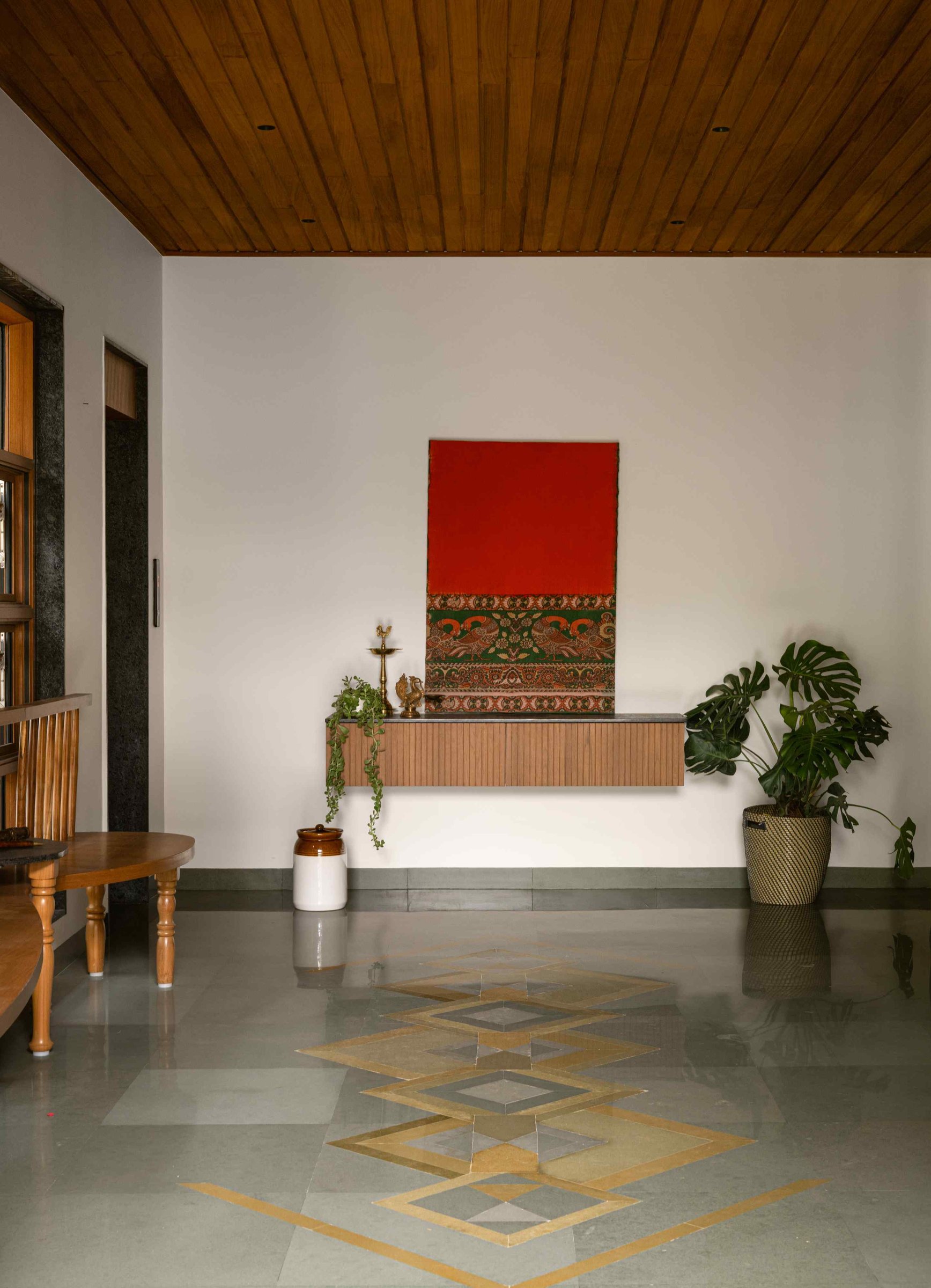 The foyer: slatted wood overhead, a brass-and-stone geometric inlay underfoot, and a textile artwork that locates the home culturally without overt signalling