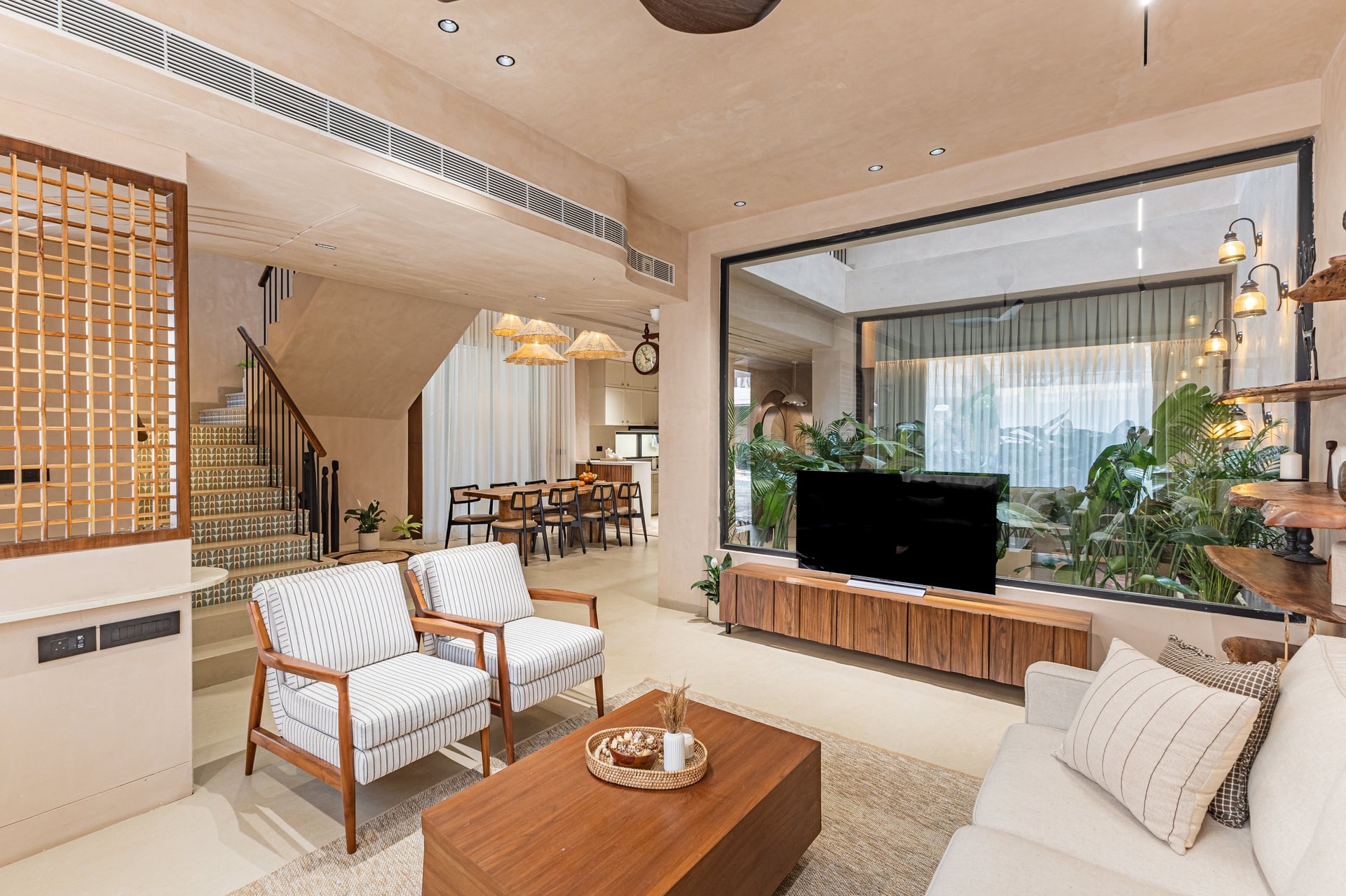 The living room opens through a wide picture window, the slatted wood console echoing the jaali screen opposite
