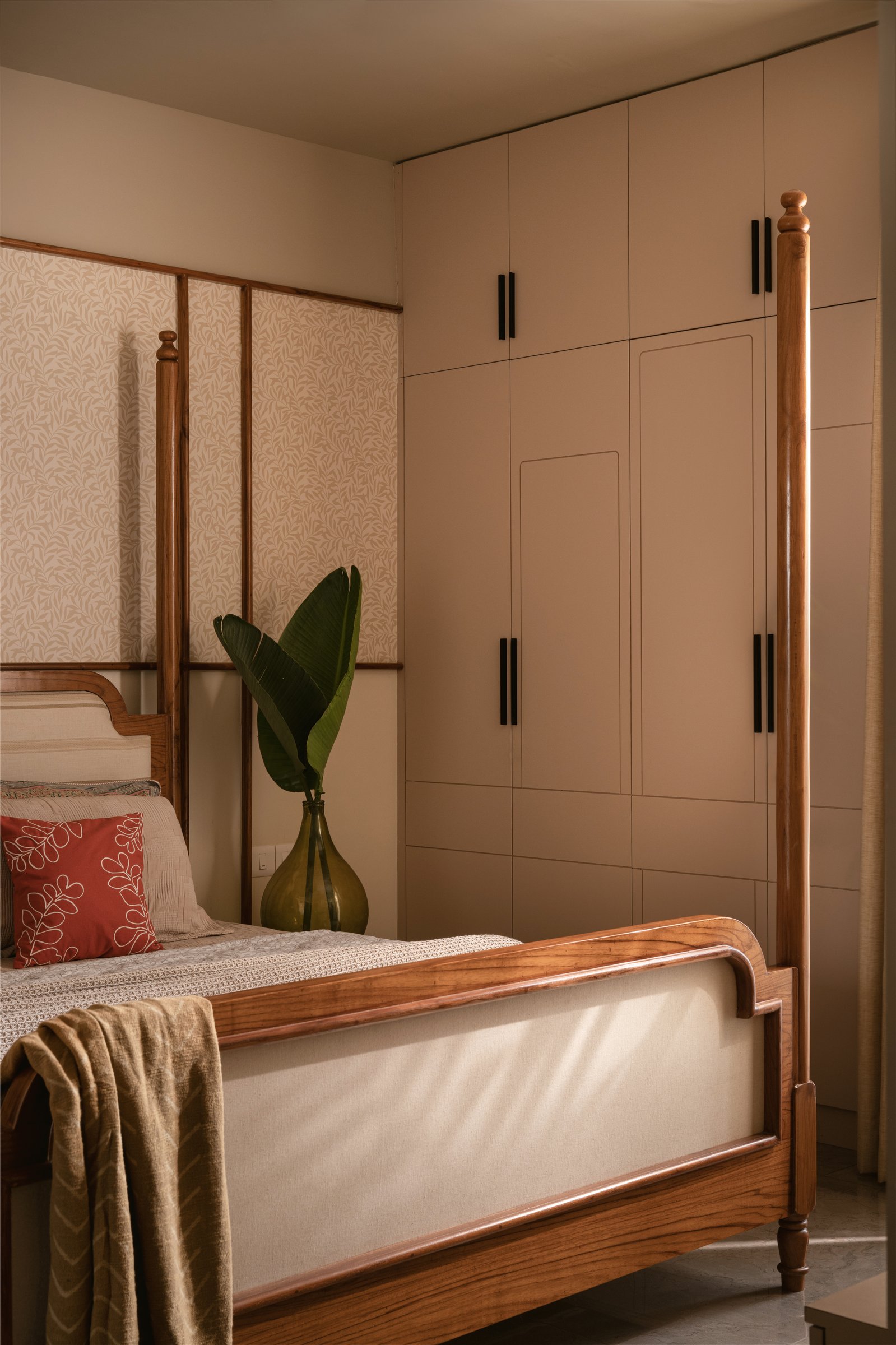 The second bedroom: a honey-toned four-poster bed against a leaf-motif wallpaper, the home's most pastoral register