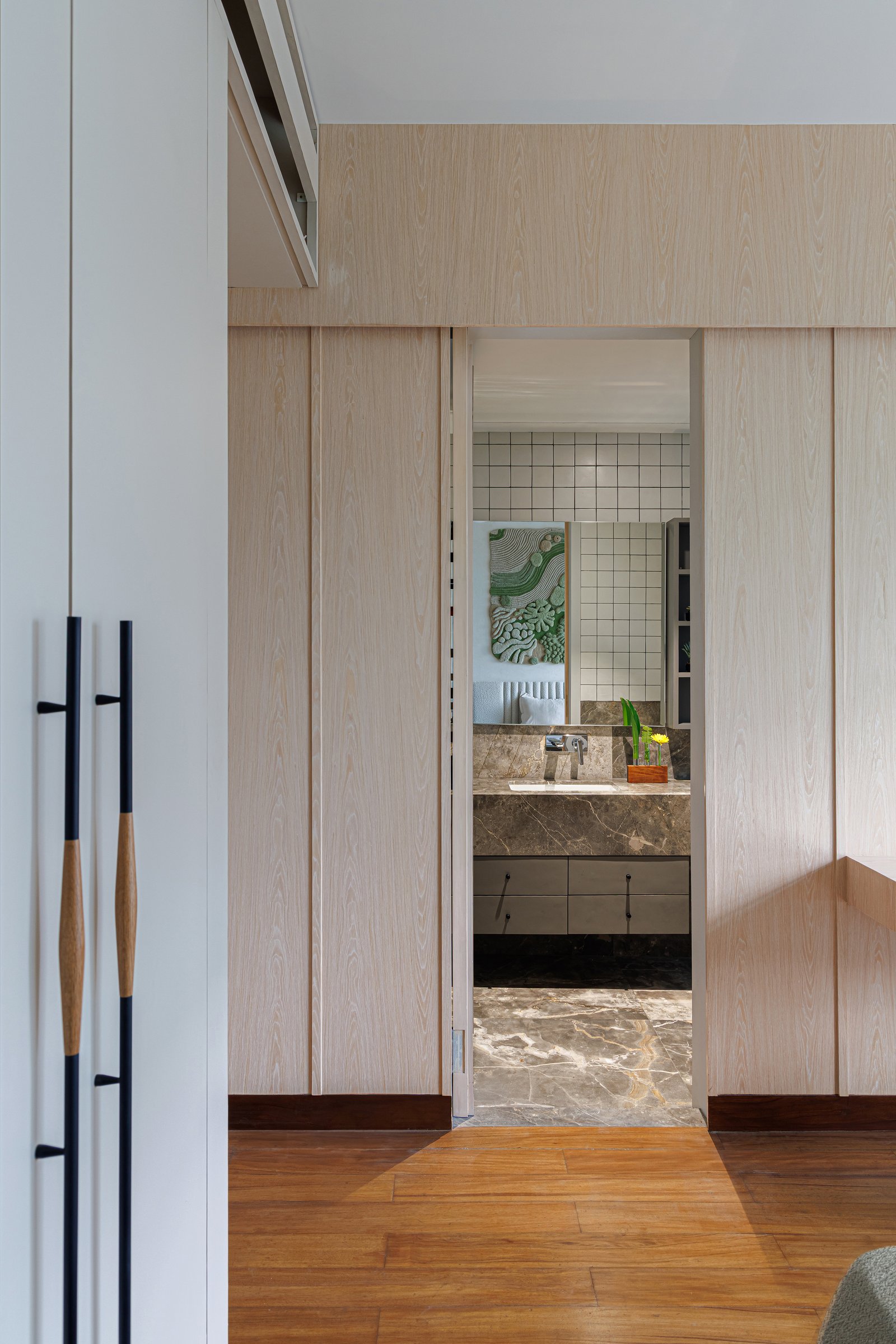 A pocket sliding panel opens to an ensuite bathroom, where a grey-veined marble vanity and a grid of white wall tiles wait beyond the threshold