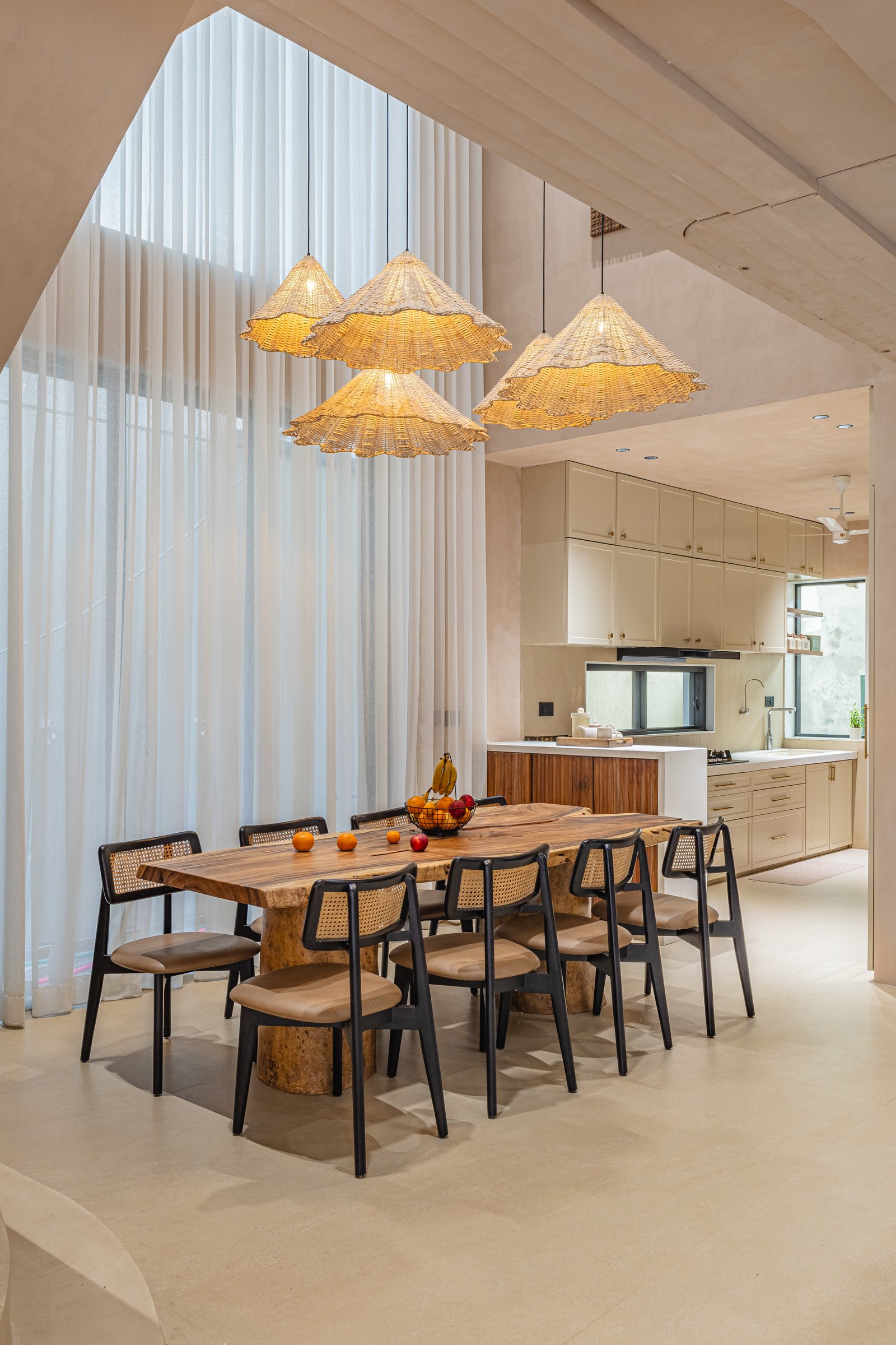 The dining area, where a double-height curtain wall lets the woven pendants behave as a single suspended composition