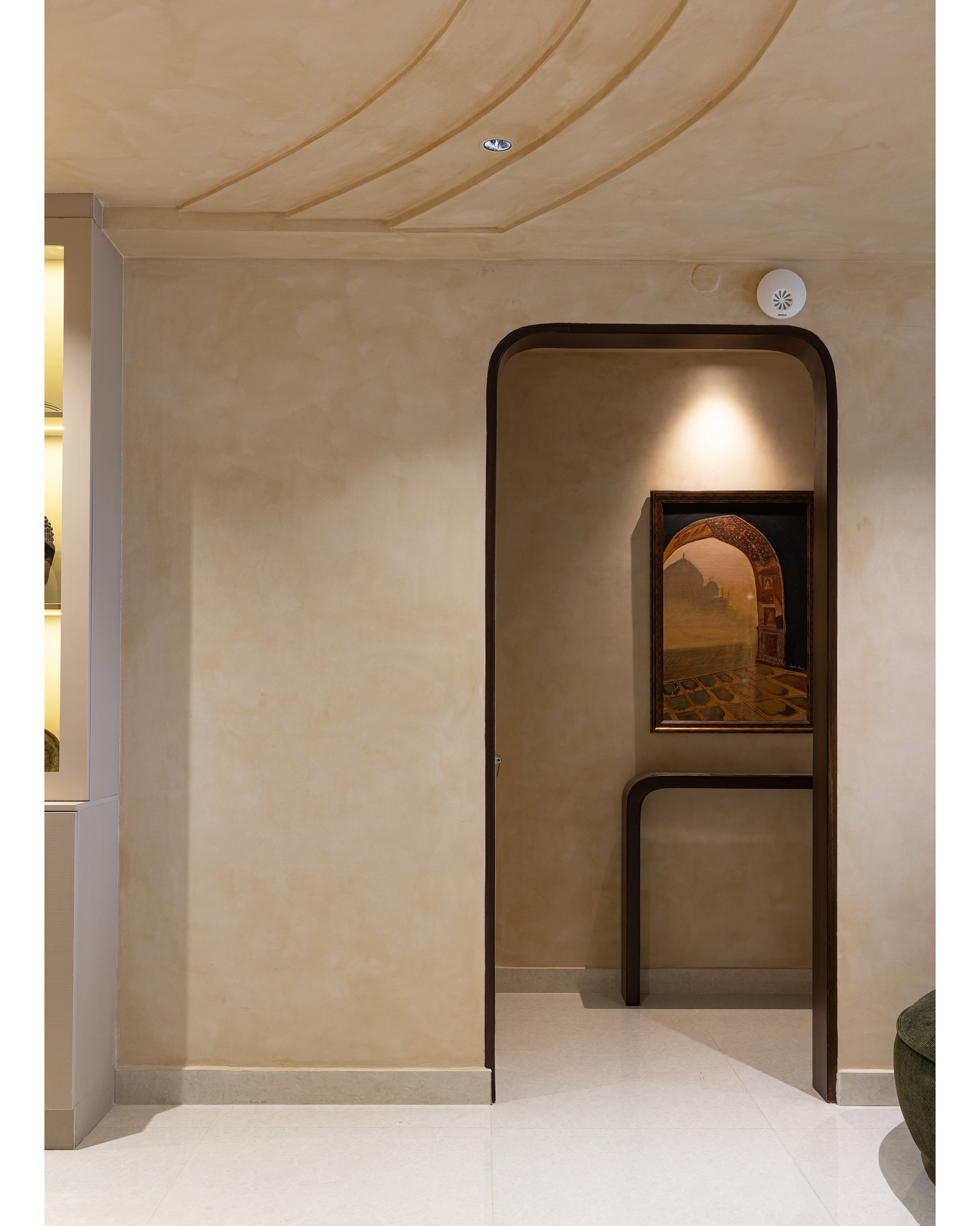 The arrival vestibule, where a rounded portal frames a small Mughal-arch painting and a curved console, introducing the home's limewash language