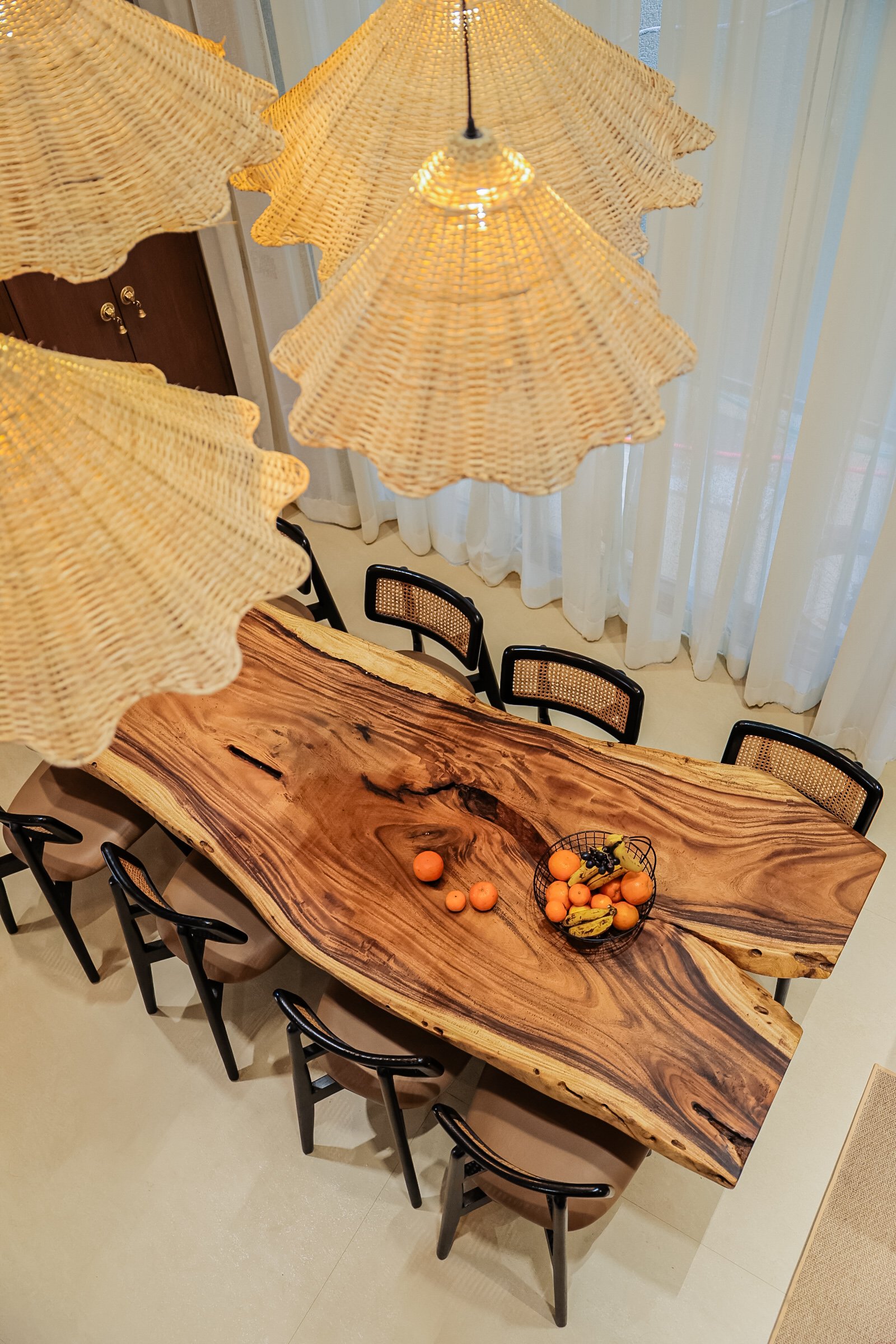 The live-edge dining slab, the home's most expressive object, scaled against a cluster of woven pendants