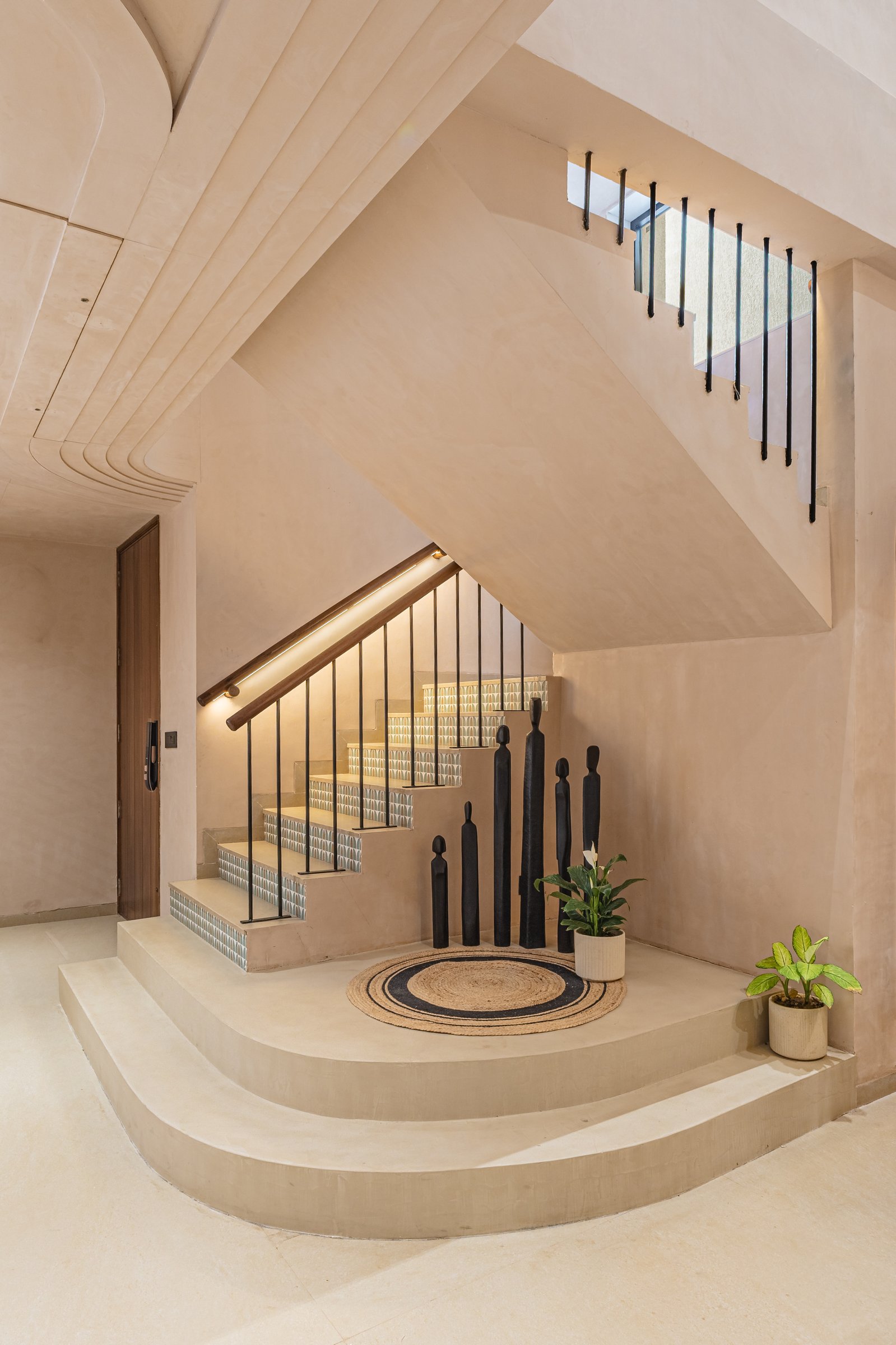 The staircase landing, where a curved plinth and a cluster of black figurines perform the work of a foyer