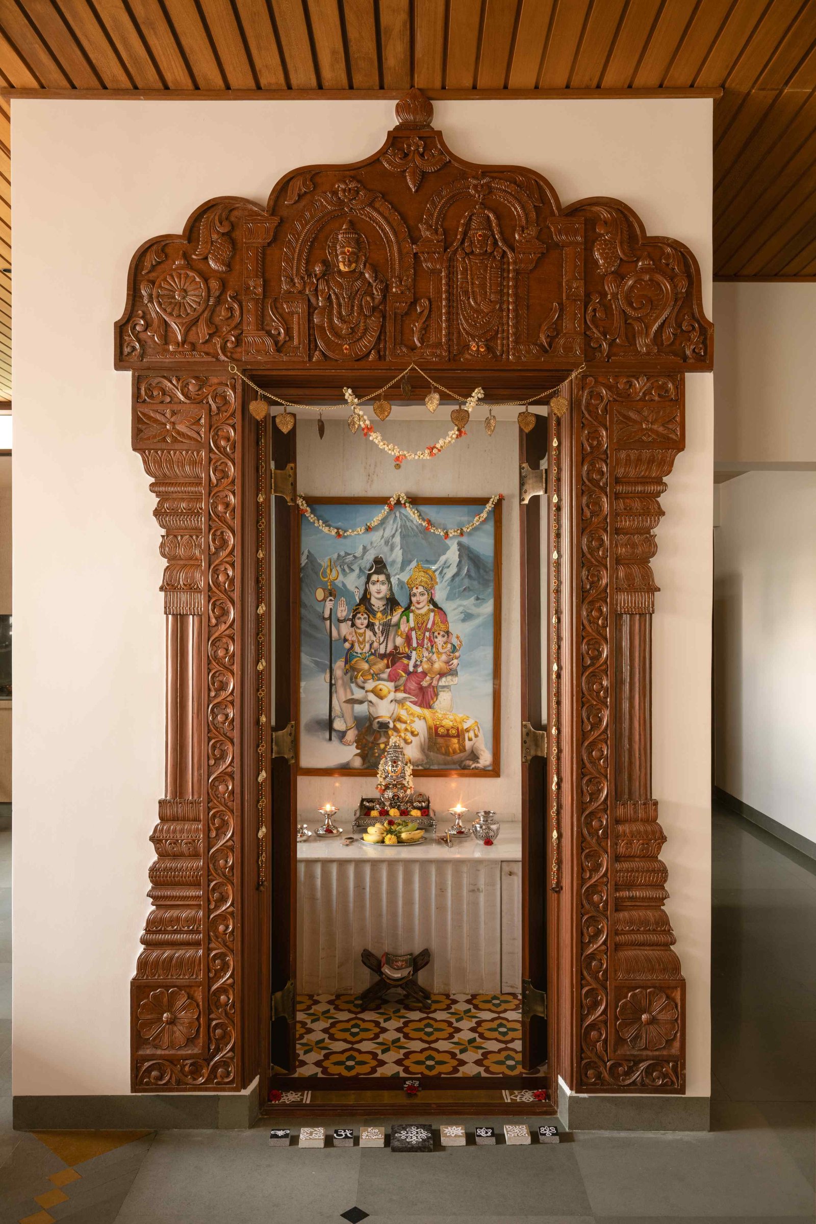 The pooja, framed by a carved wooden doorway and floored in patterned cement tile, holds its tradition with quiet seriousness