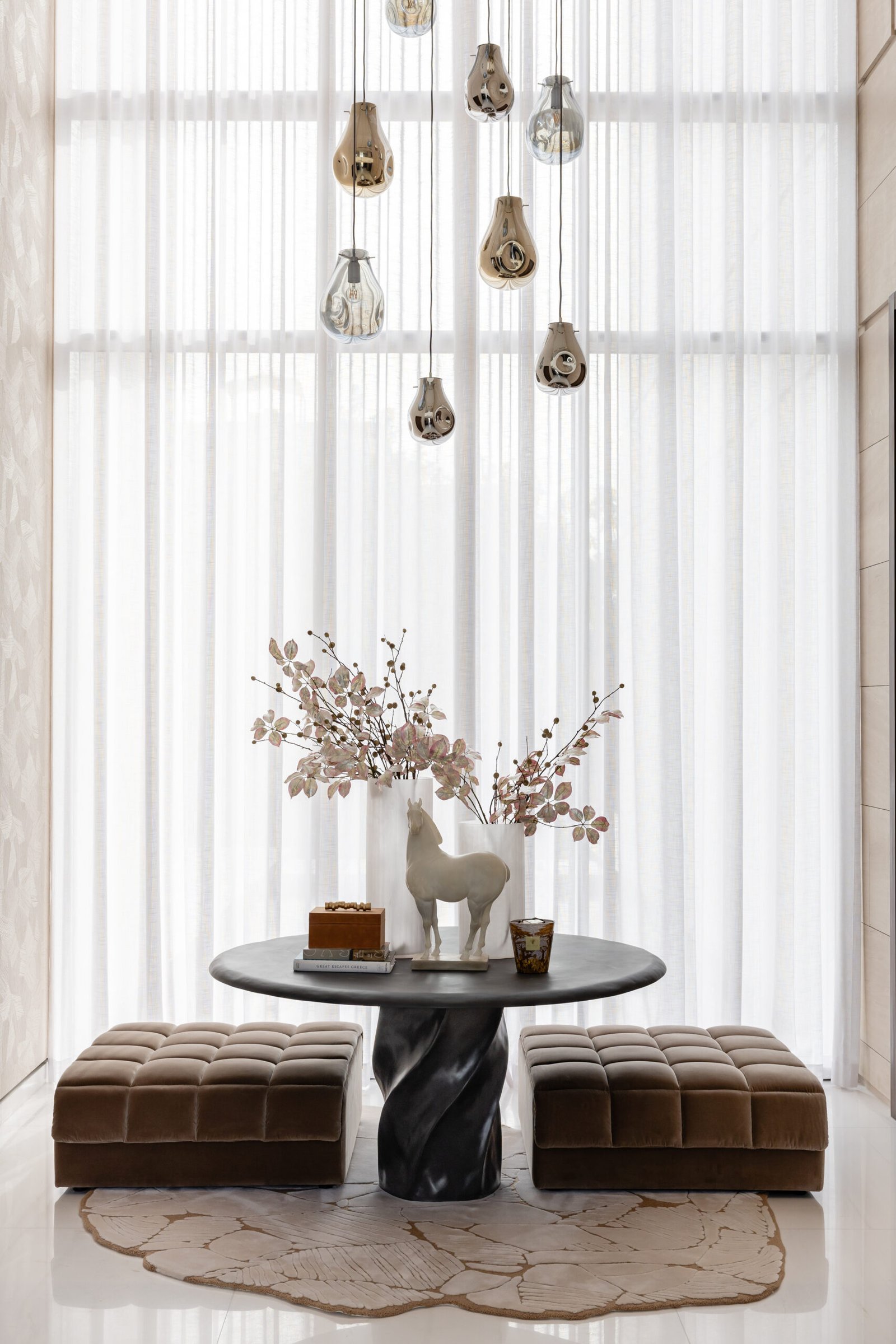 Beneath the double-height void, a twisted-base table and tufted ottomans are anchored by a cascade of mirrored glass pendants