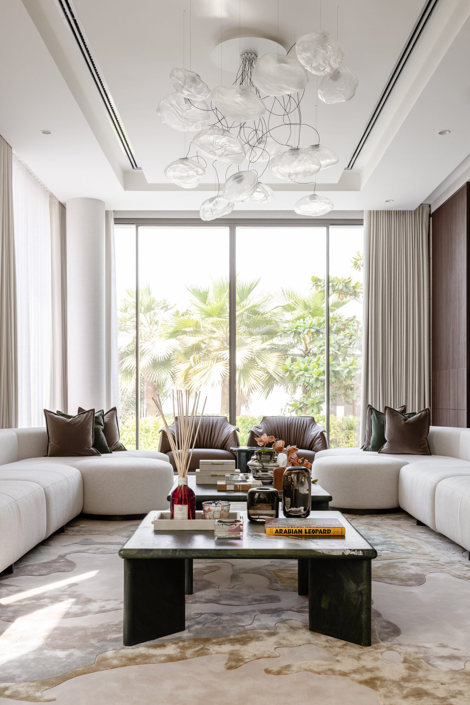 The cloud-like glass chandelier, the room's single permitted extravagance, suspended against floor-to-ceiling garden views