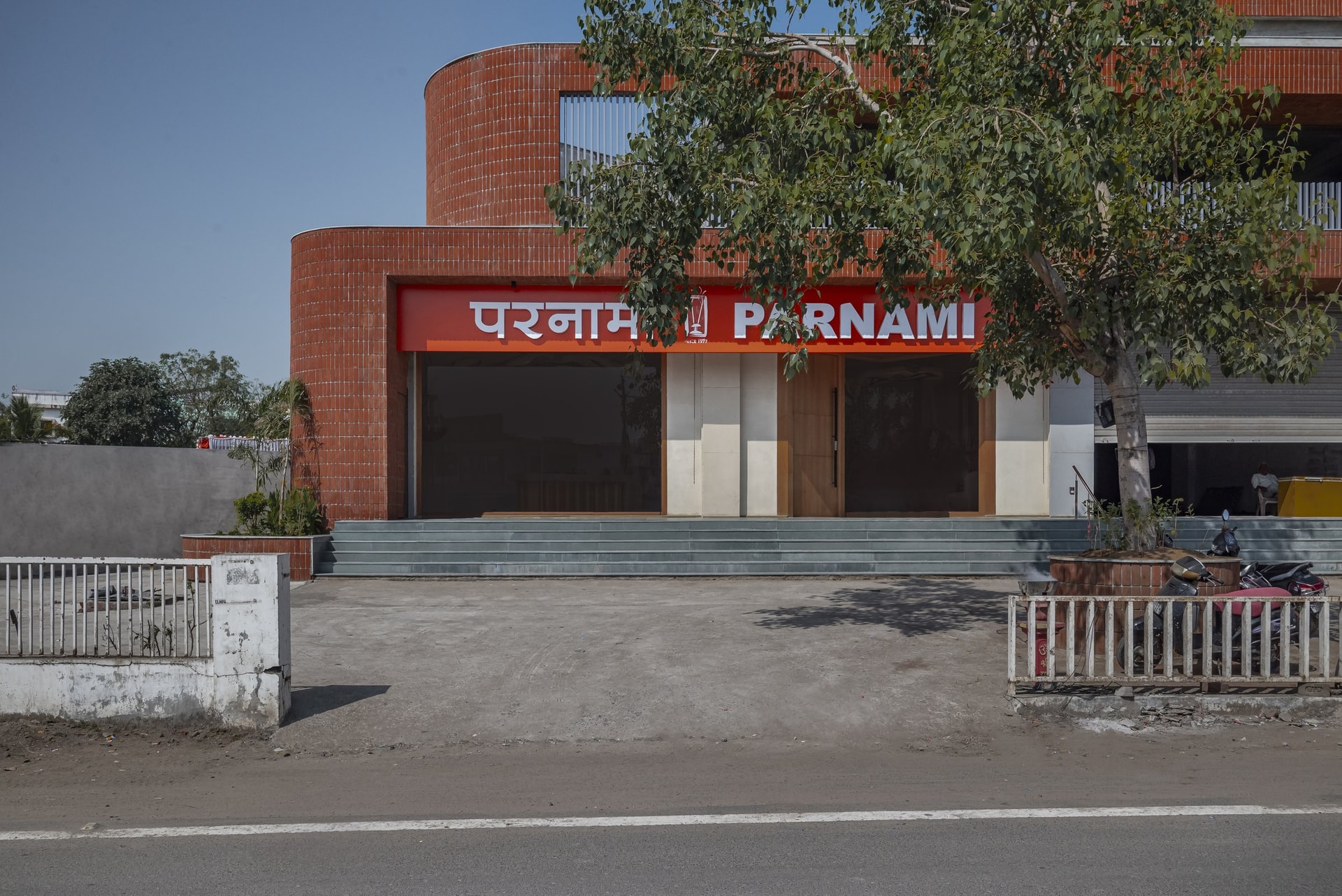 The Vadodara facade: red-brick curves wrap the triangular site, the Parnami wordmark held within a single horizontal band