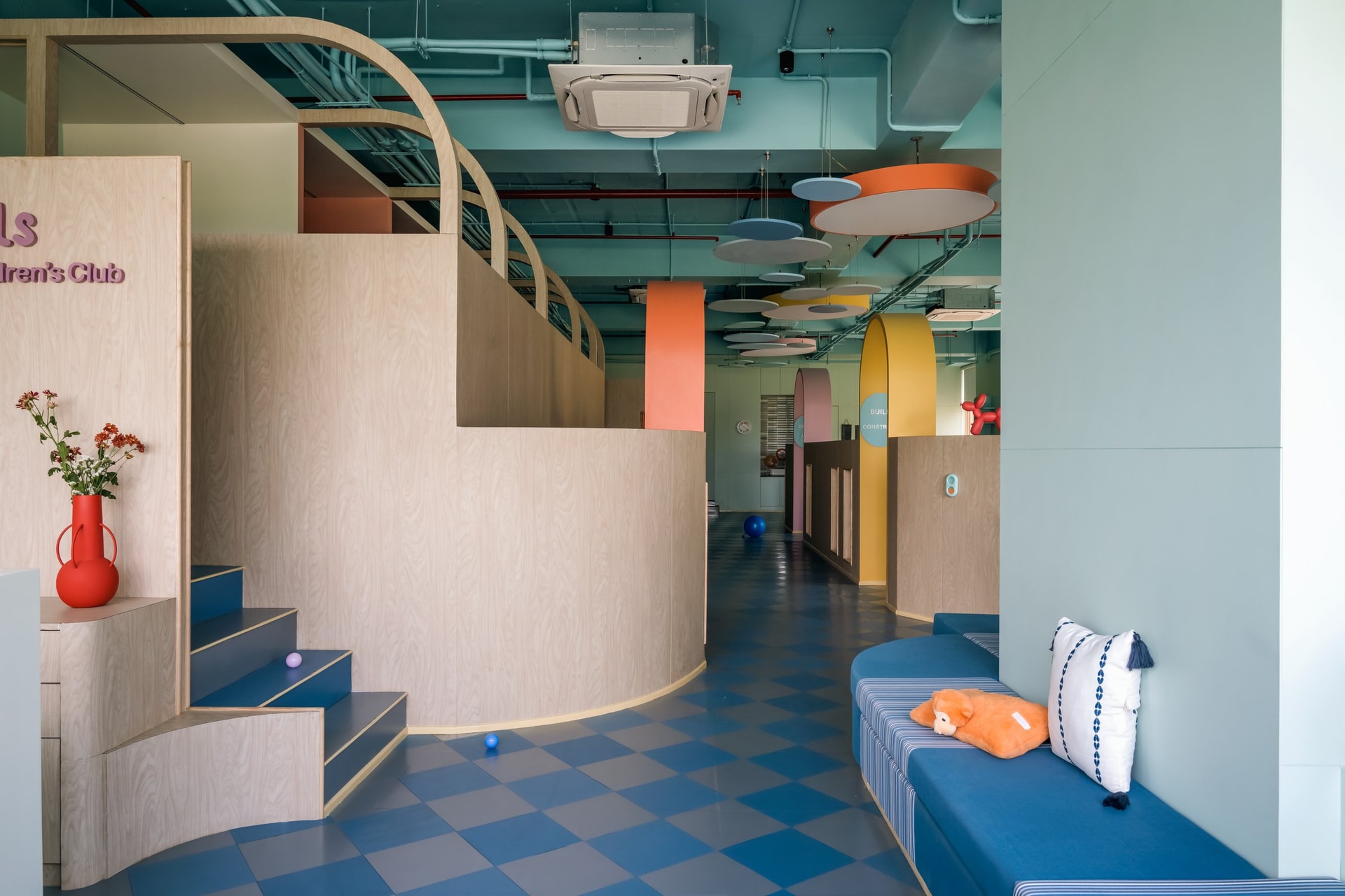 The central commons: a curved plywood staircase, a striped blue daybed for caregivers, and circular acoustic baffles softening the open volume