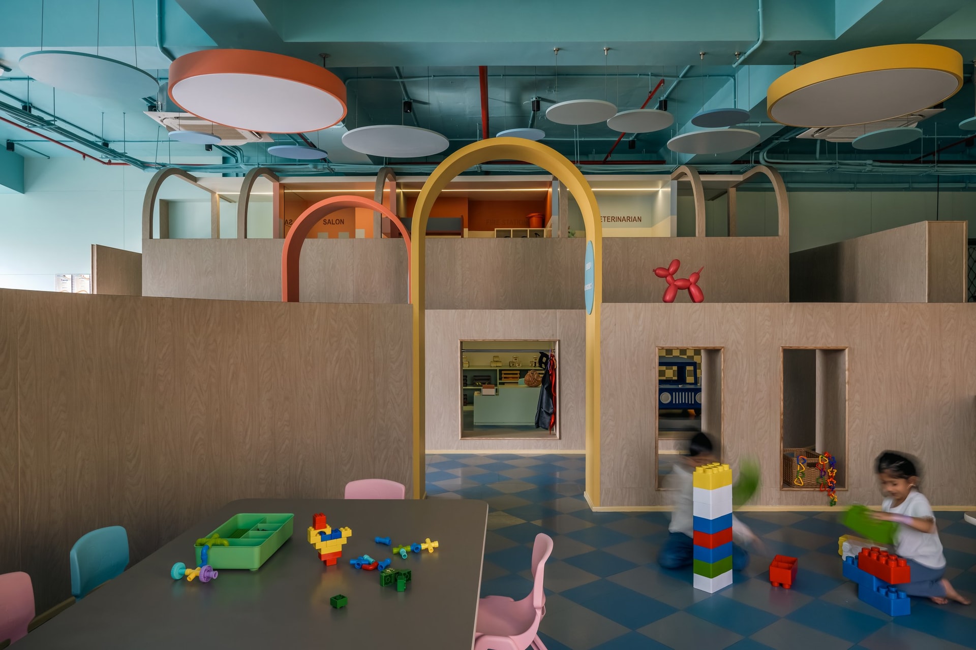 Low plywood partitions with cut-out windows preserve sightlines across the pretend-play zone