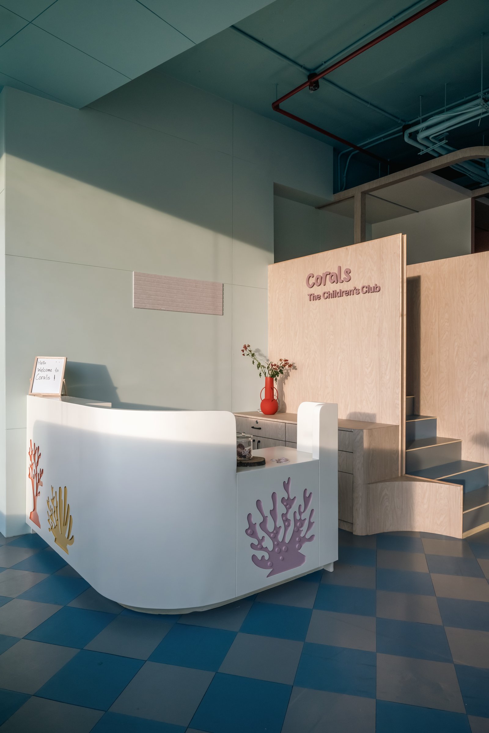 The reception desk, fronted with cut-out coral motifs in mauve, ochre, and burnt orange, sets the visual vocabulary of the entire club