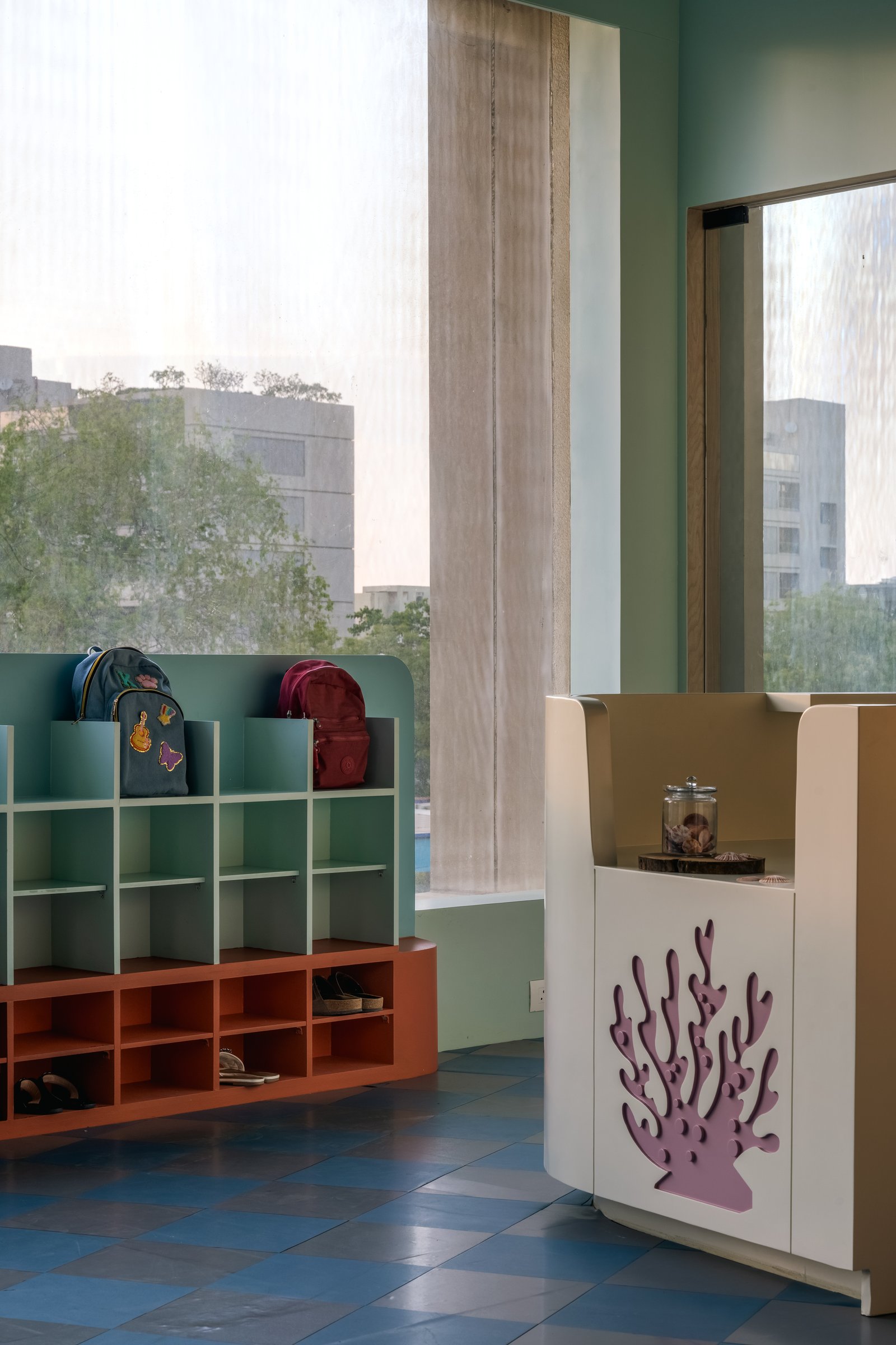 The cubby unit in mint and terracotta, with a sculptural coral-leaf signature on the adjacent counter