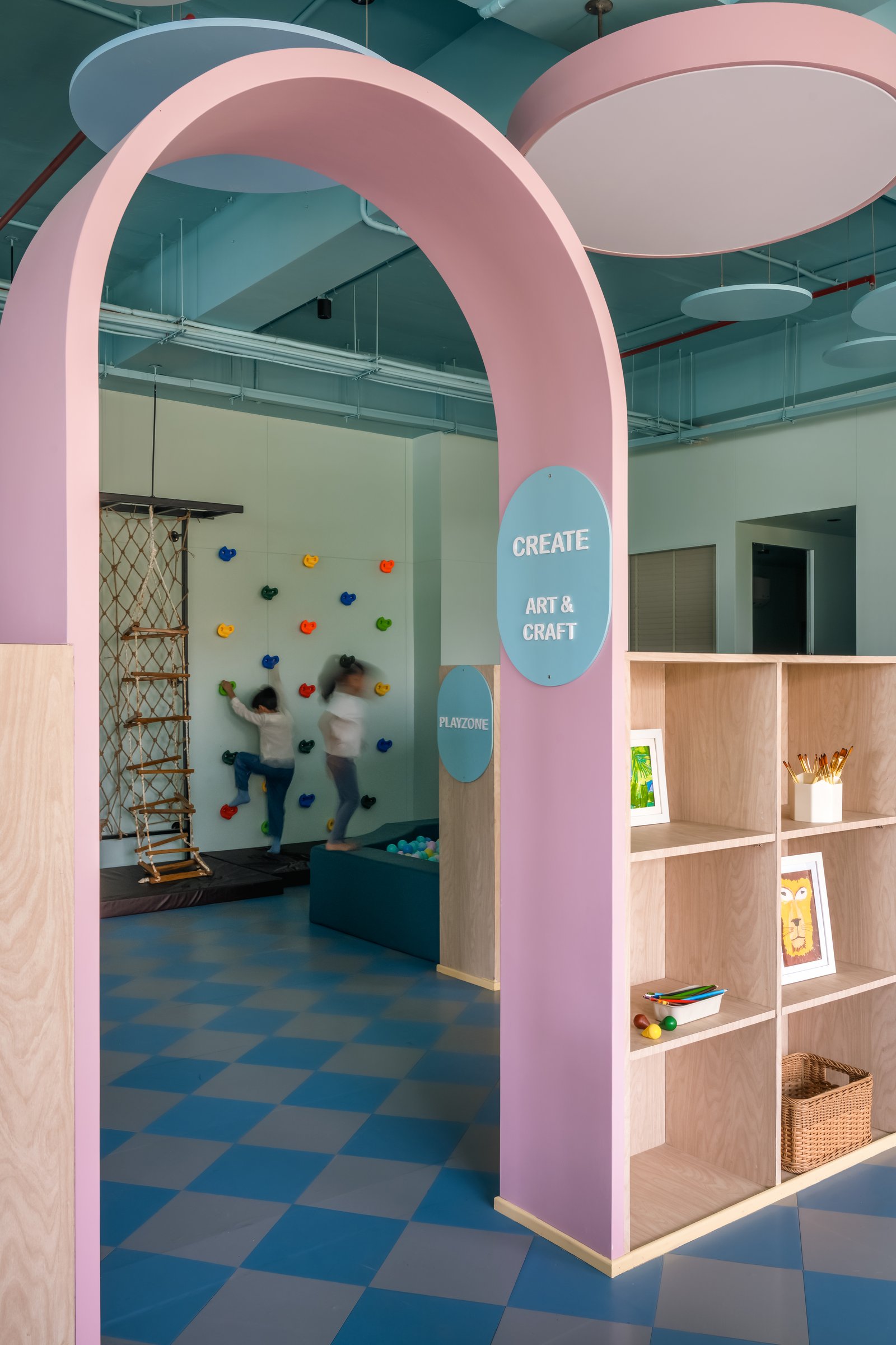 The pink arch leading to active play, where climbing wall and art shelves share a single threshold