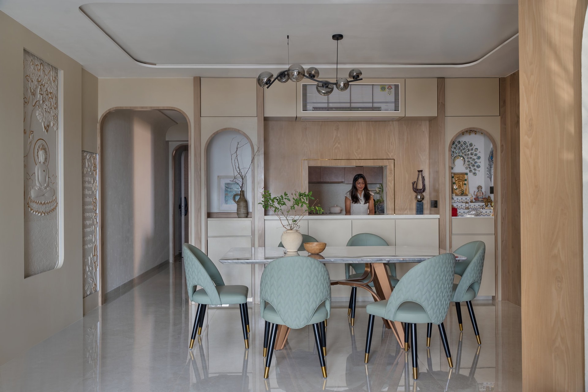 The dining table on its sculptural wood-and-copper base, pale chairs flanking the pass-through kitchen