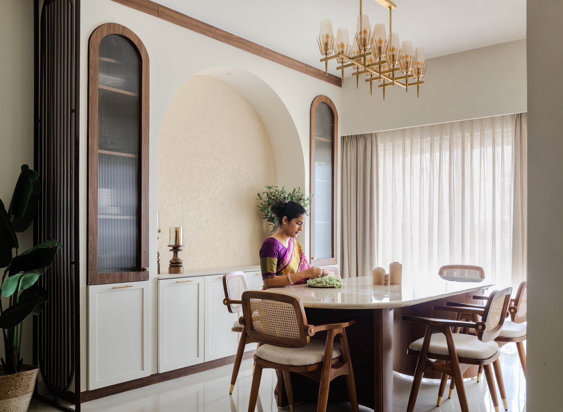 The stone-topped oval table and cane-backed chairs, lit by a brass chandelier with frosted shades