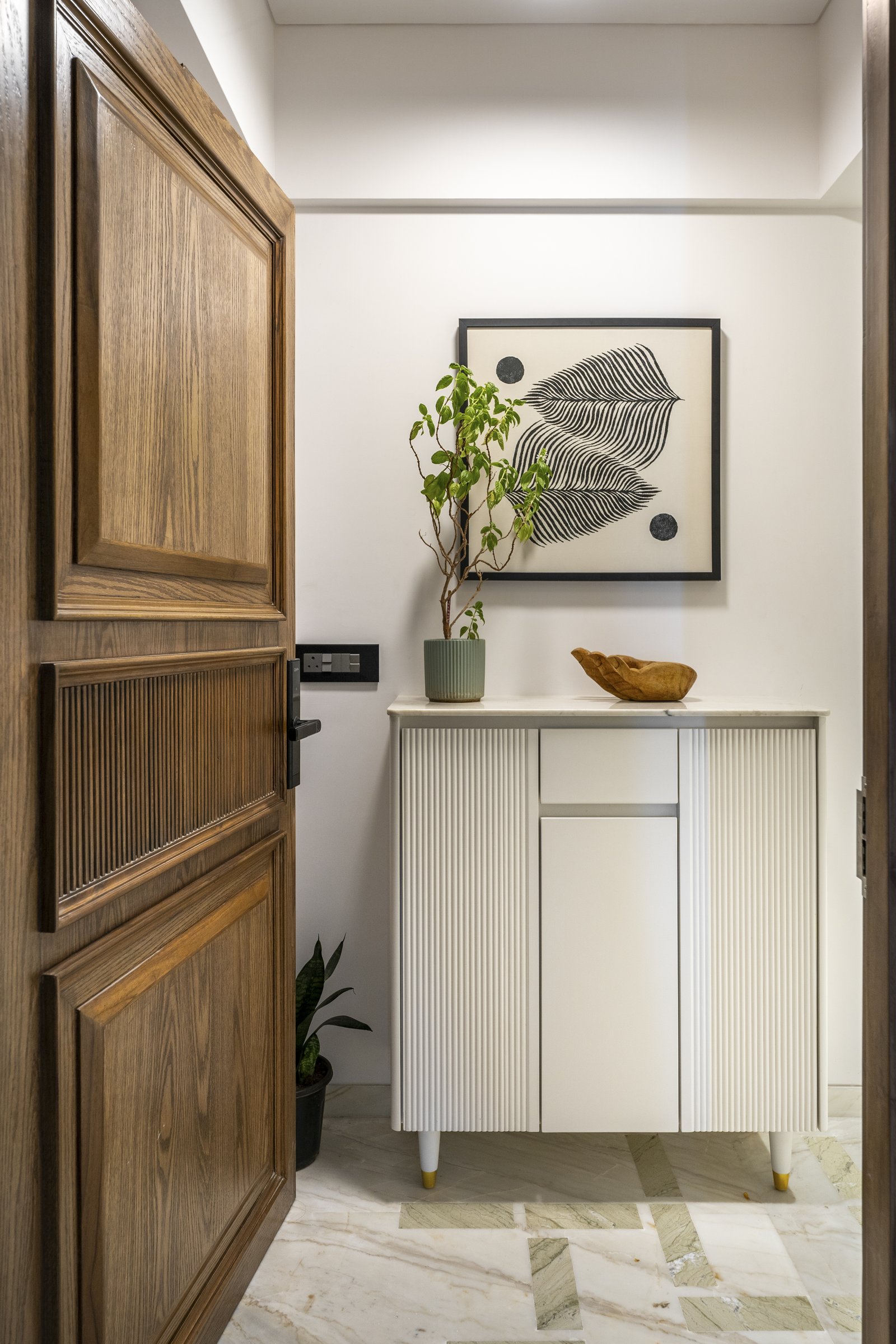 The foyer: a panelled oak door, a fluted ivory console, and a marble inlay floor that introduces the home's green-veined stone before the living room reveals it