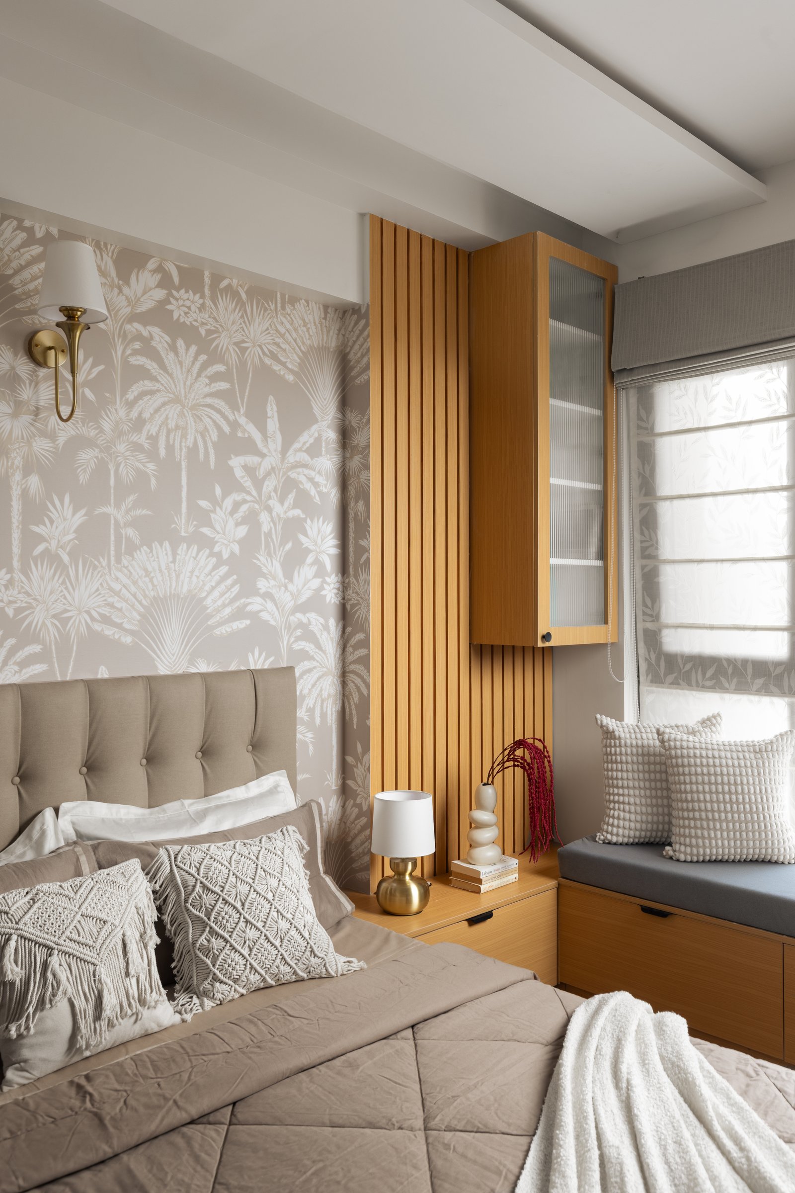 The guest bedroom opens with a tufted headboard, palm-print wallpaper and a wood-clad window seat