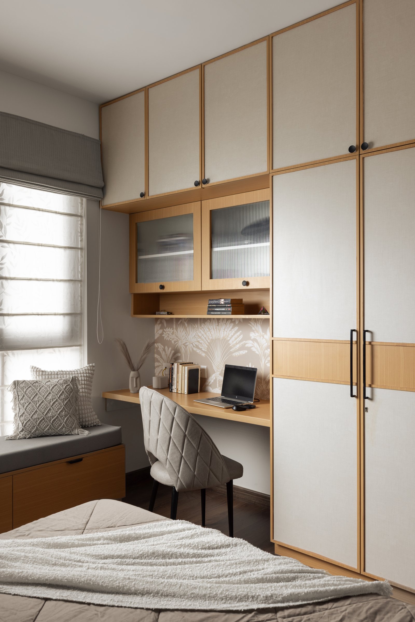 The same room's vanishing workspace: a built-in desk beneath fluted-glass uppers, with the window seat extending alongside