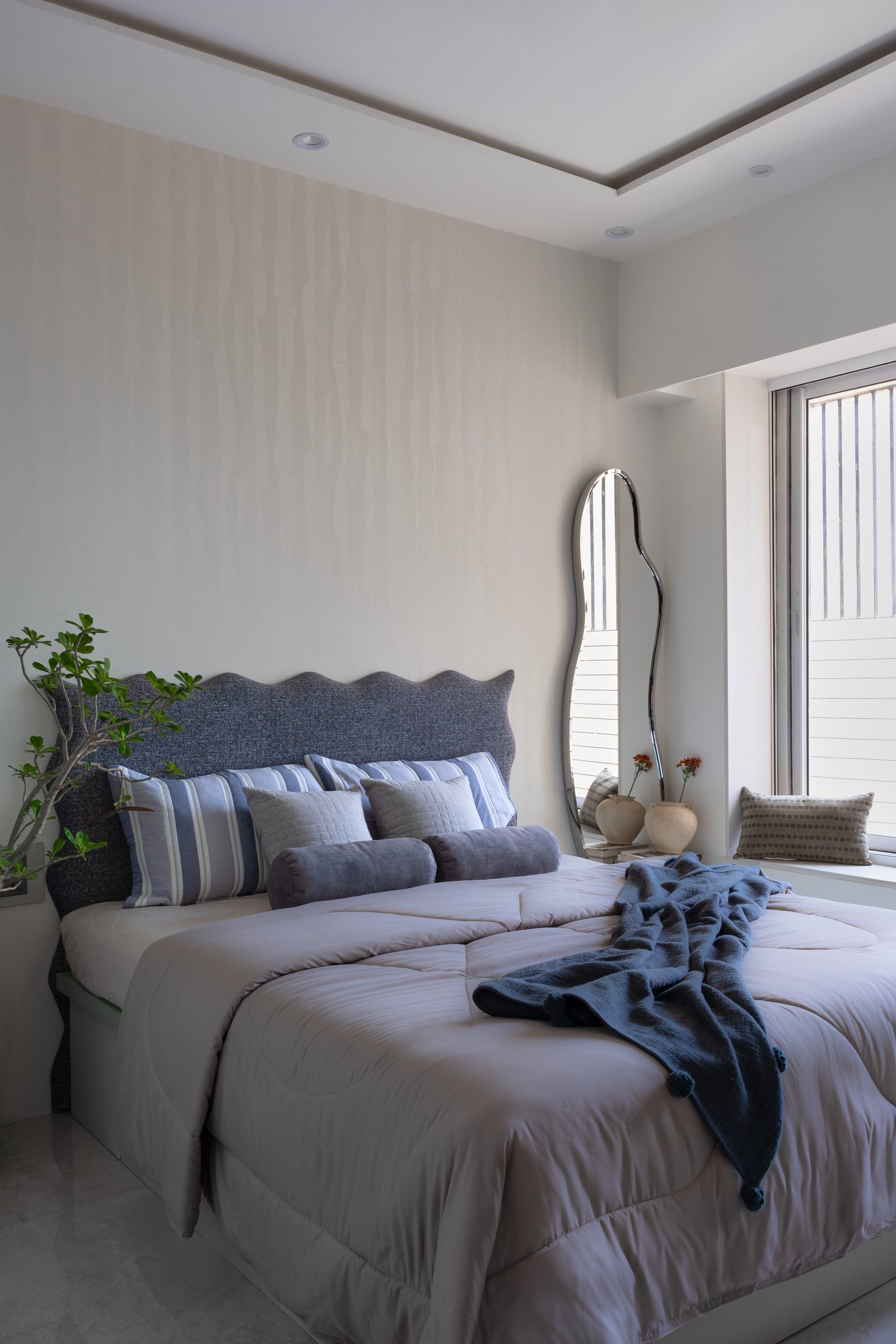 The second bedroom: a scalloped slate-blue headboard and a freeform mirror in the window bay