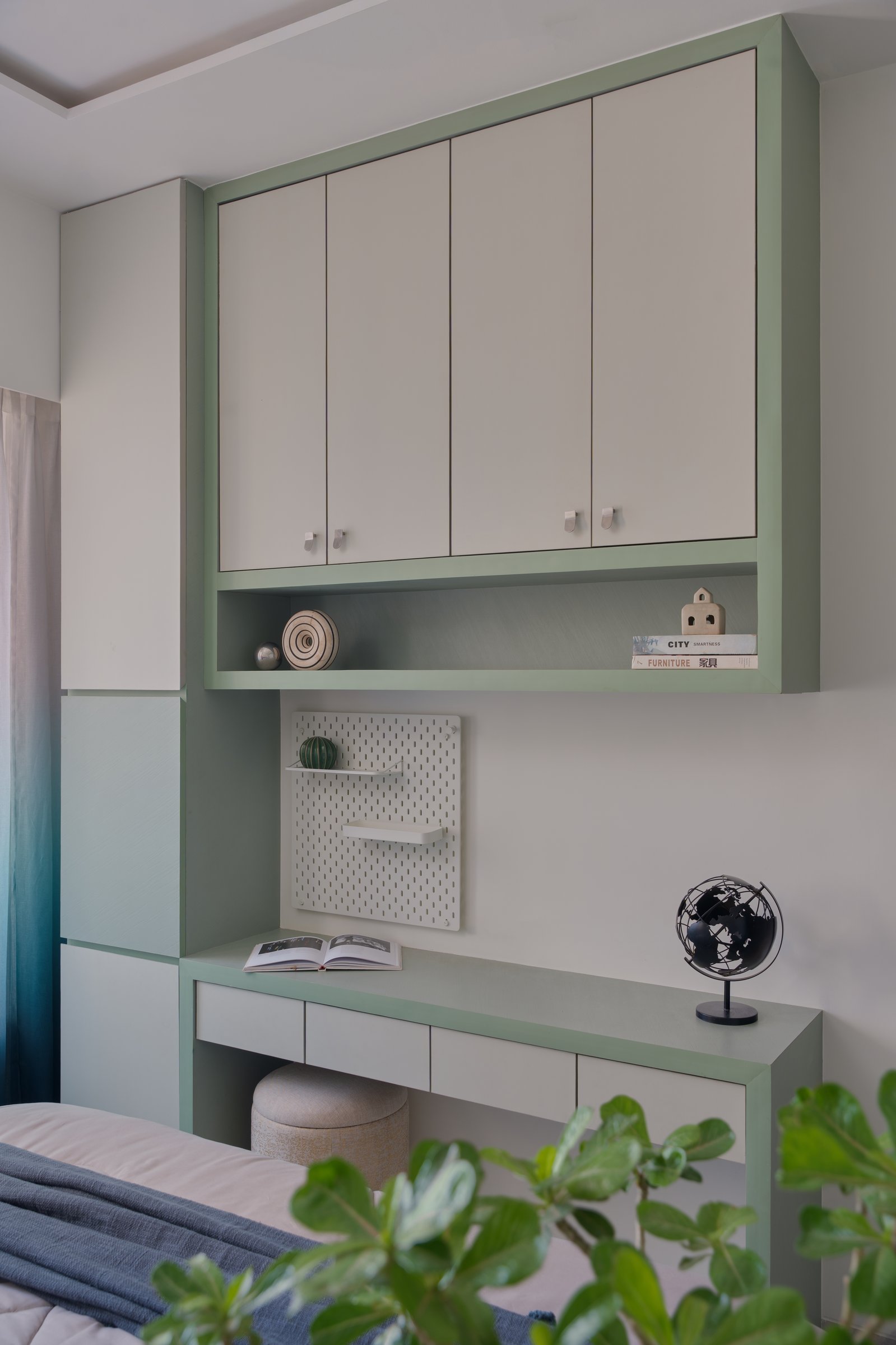 A sage-green study unit organises cabinetry, display ledge, and writing desk into one calm composition