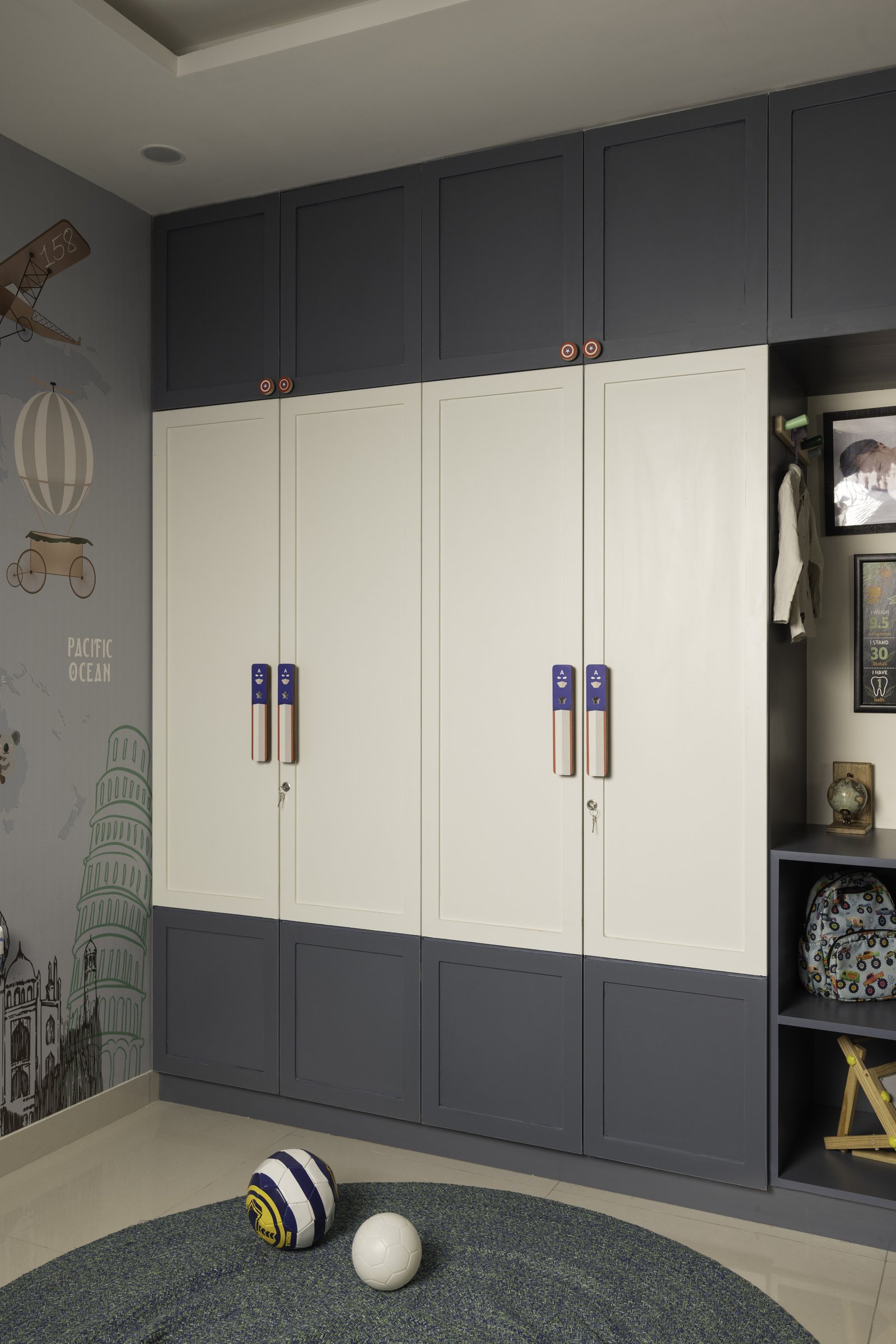 The wardrobe wall in two-tone charcoal and ivory, with custom playful handles signalling a child's room without lapsing into cartoon