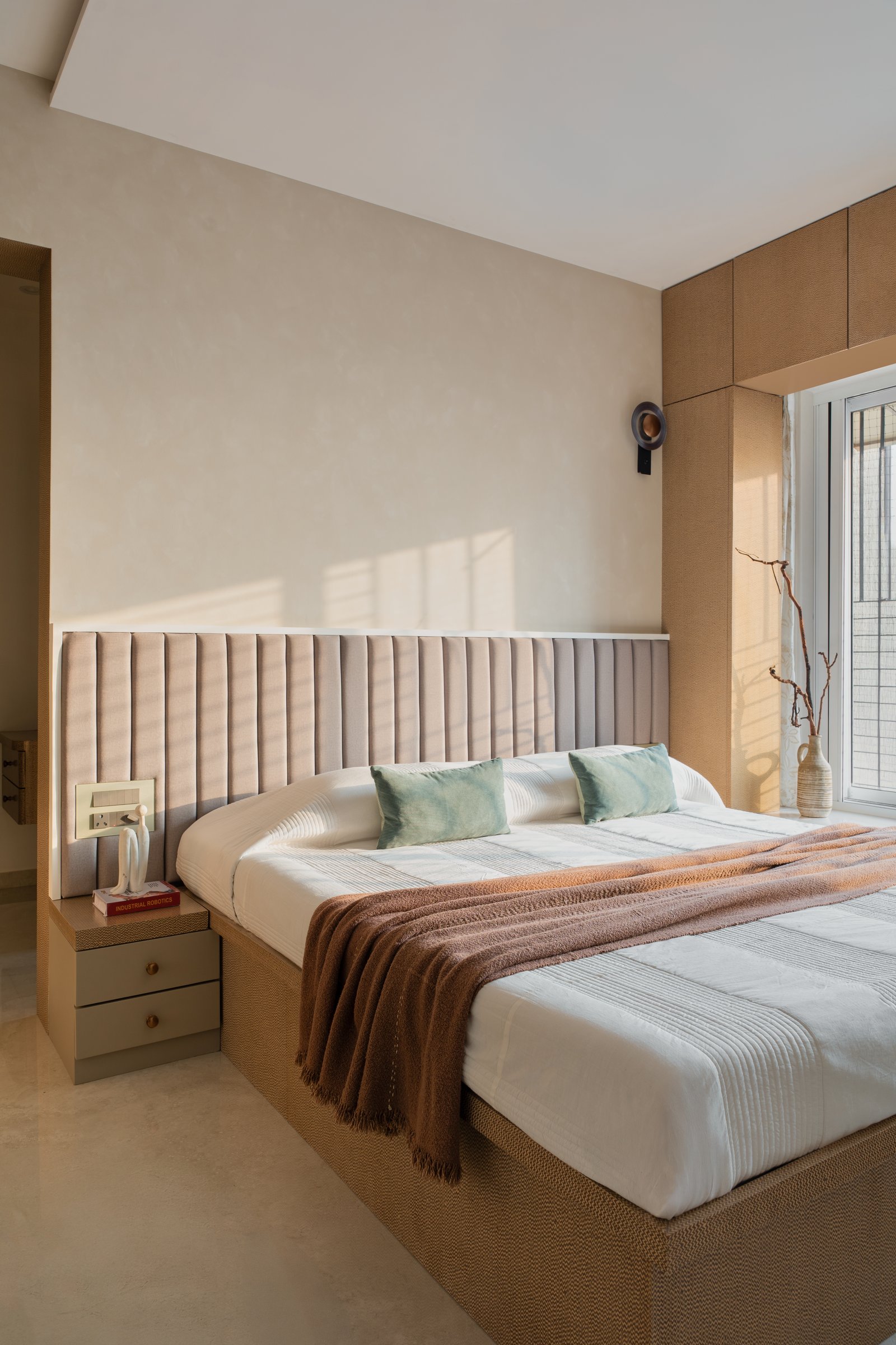 The master bedroom: a channel-tufted headboard against a soft plaster wall catches afternoon light