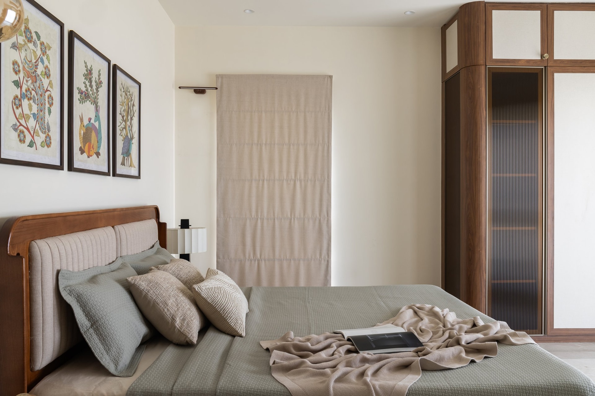 The bed wall, anchored by a curved upholstered headboard and a triptych of folk-art prints in ochre, teal, and rust