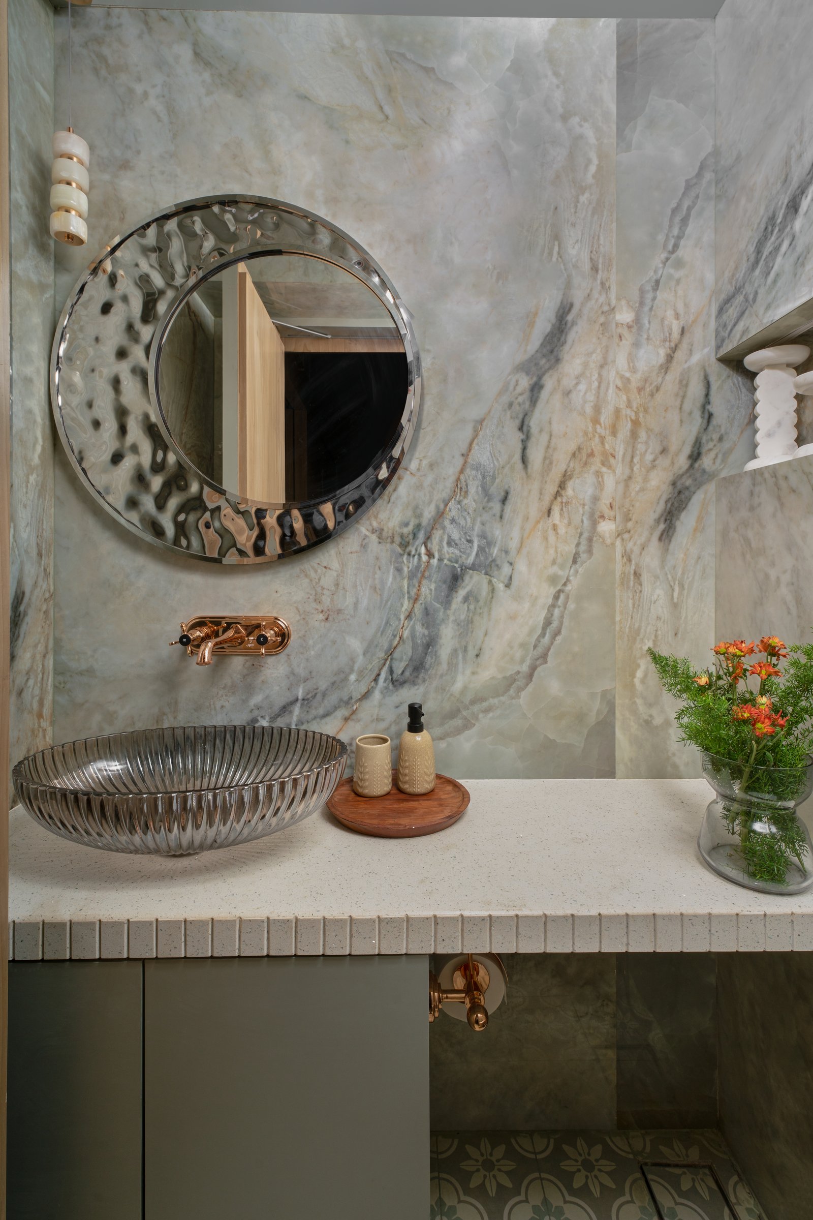 The powder room: veined stone, a hammered-glass basin, and a rose-gold tap that reads as jewellery