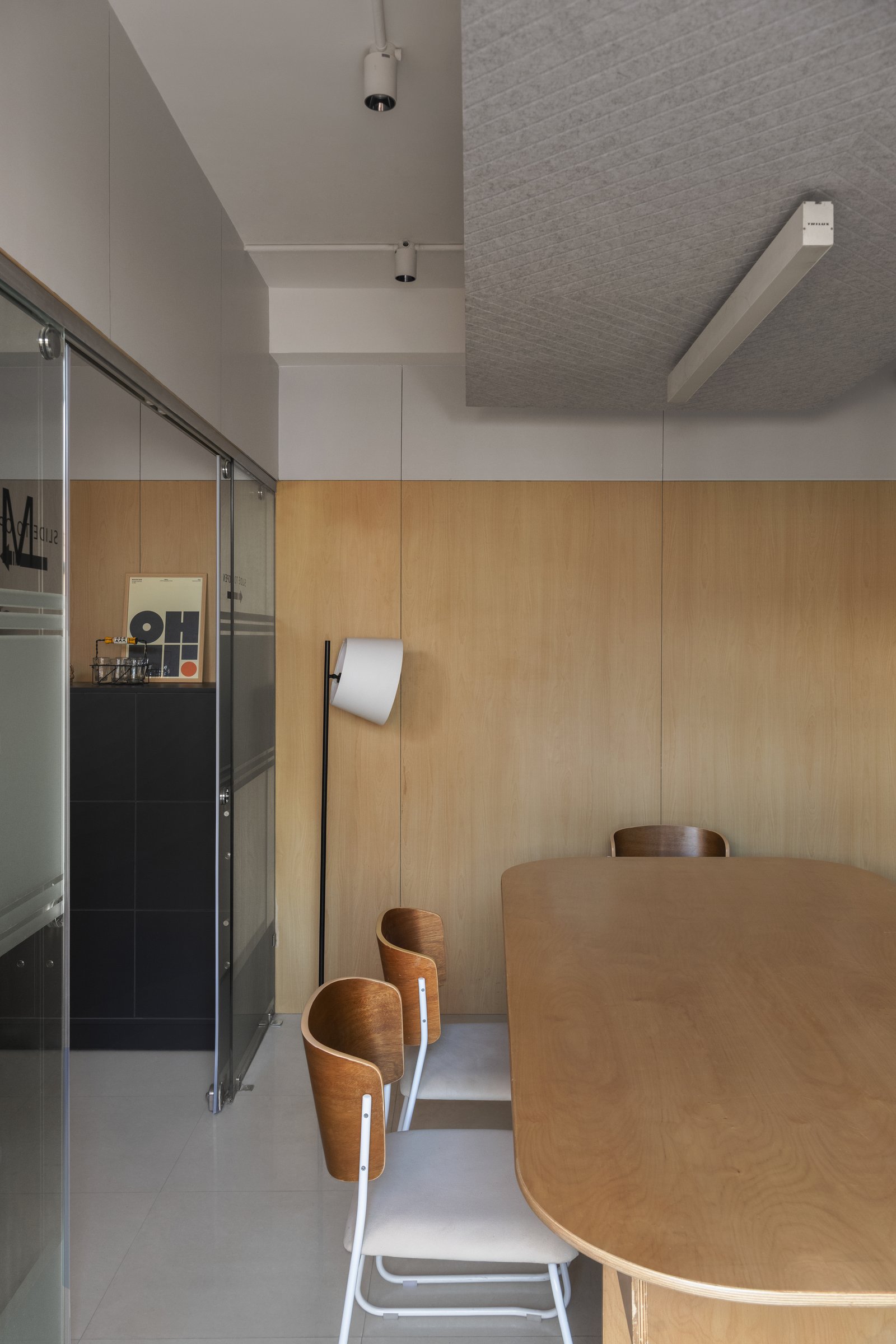 The pantry-meeting room, where a wood-panelled wall, a leaning floor lamp, and an acoustic felt ceiling shift the register toward the domestic