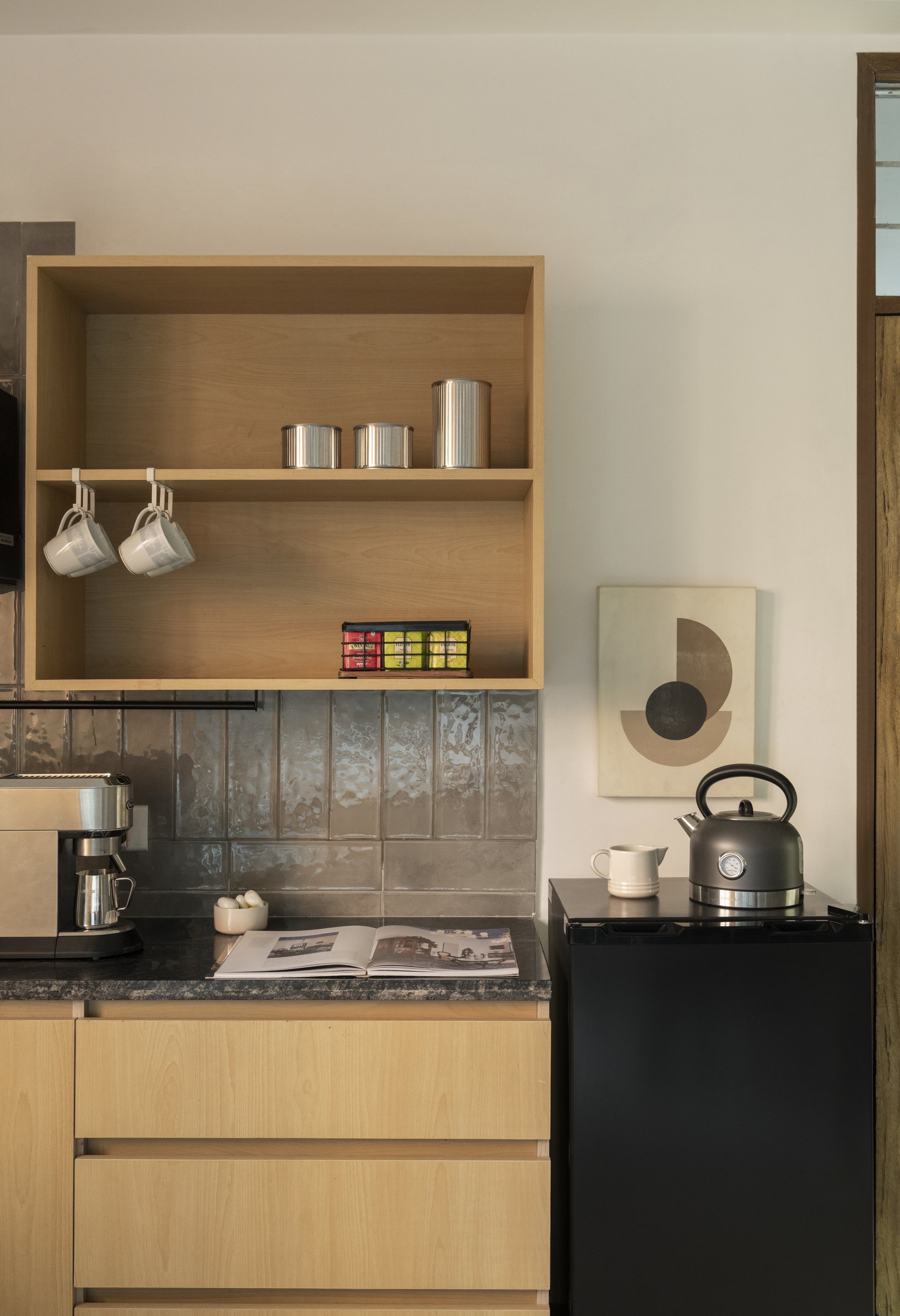 The pantry: blond birch joinery, a smoky glazed-tile backsplash, and the domestic register that runs through the entire project