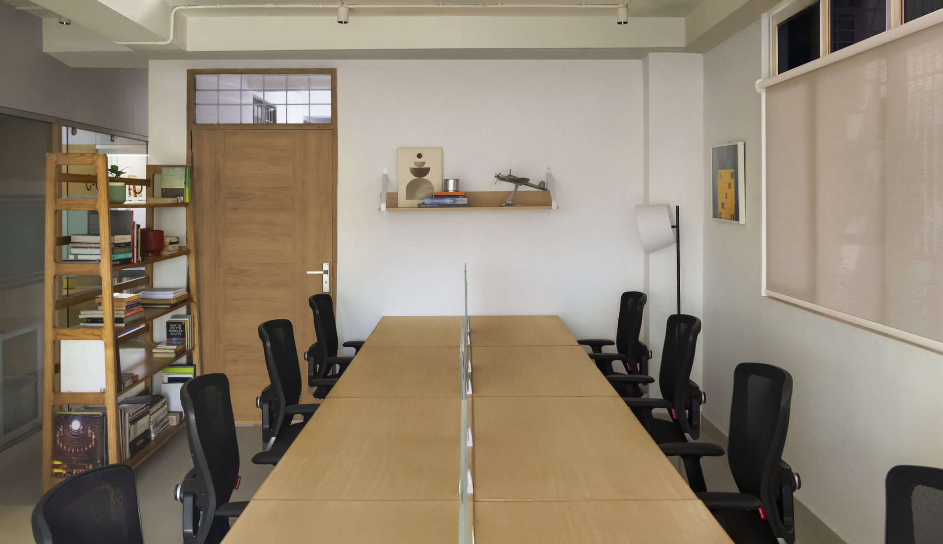 The meeting room reads as a study, a long ash-toned table divided by a slim glass spine, anchored by a tall working library