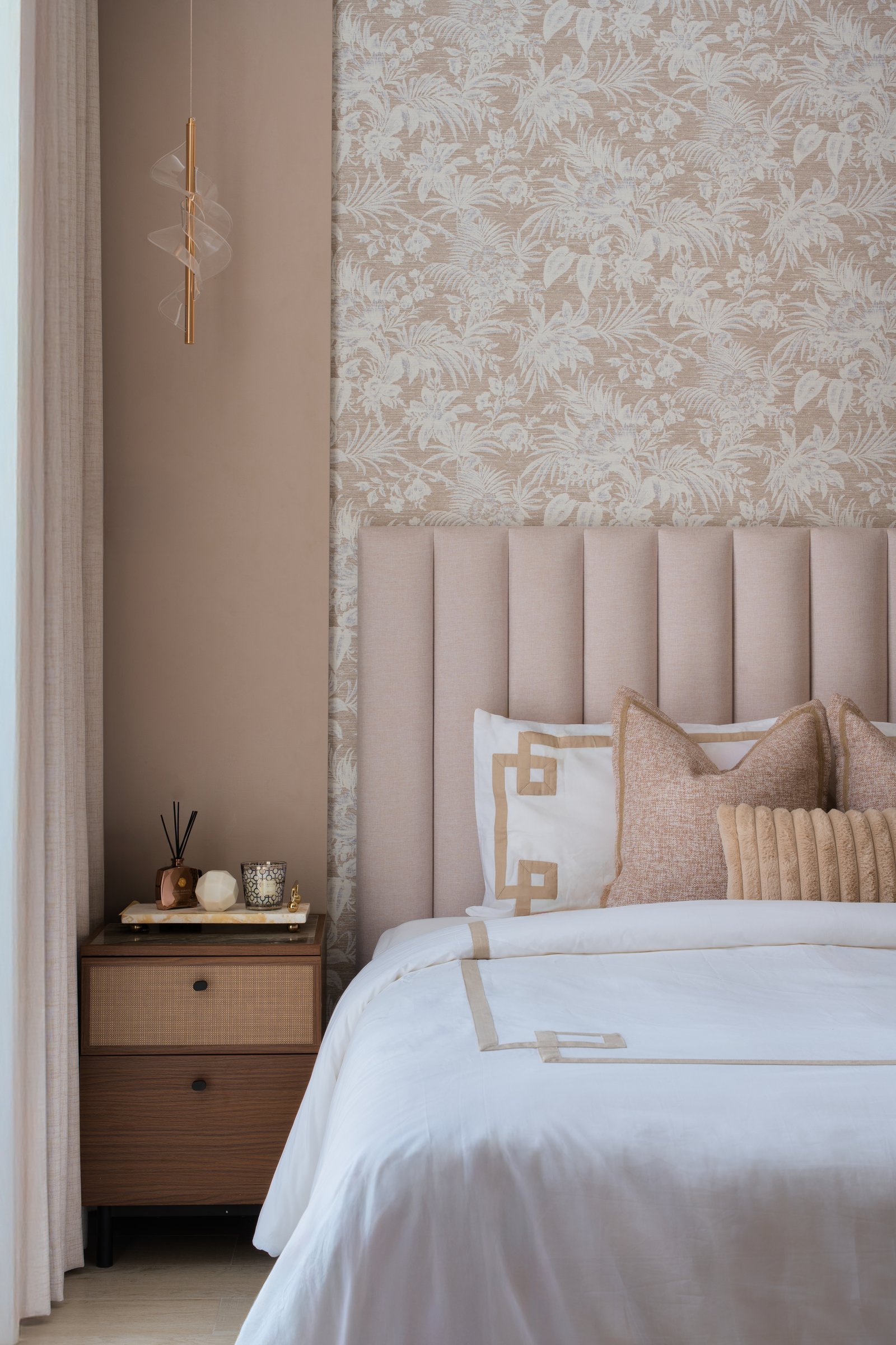 The botanical wallpaper in close view, paired with a cane-fronted bedside cabinet and a slim brass pendant