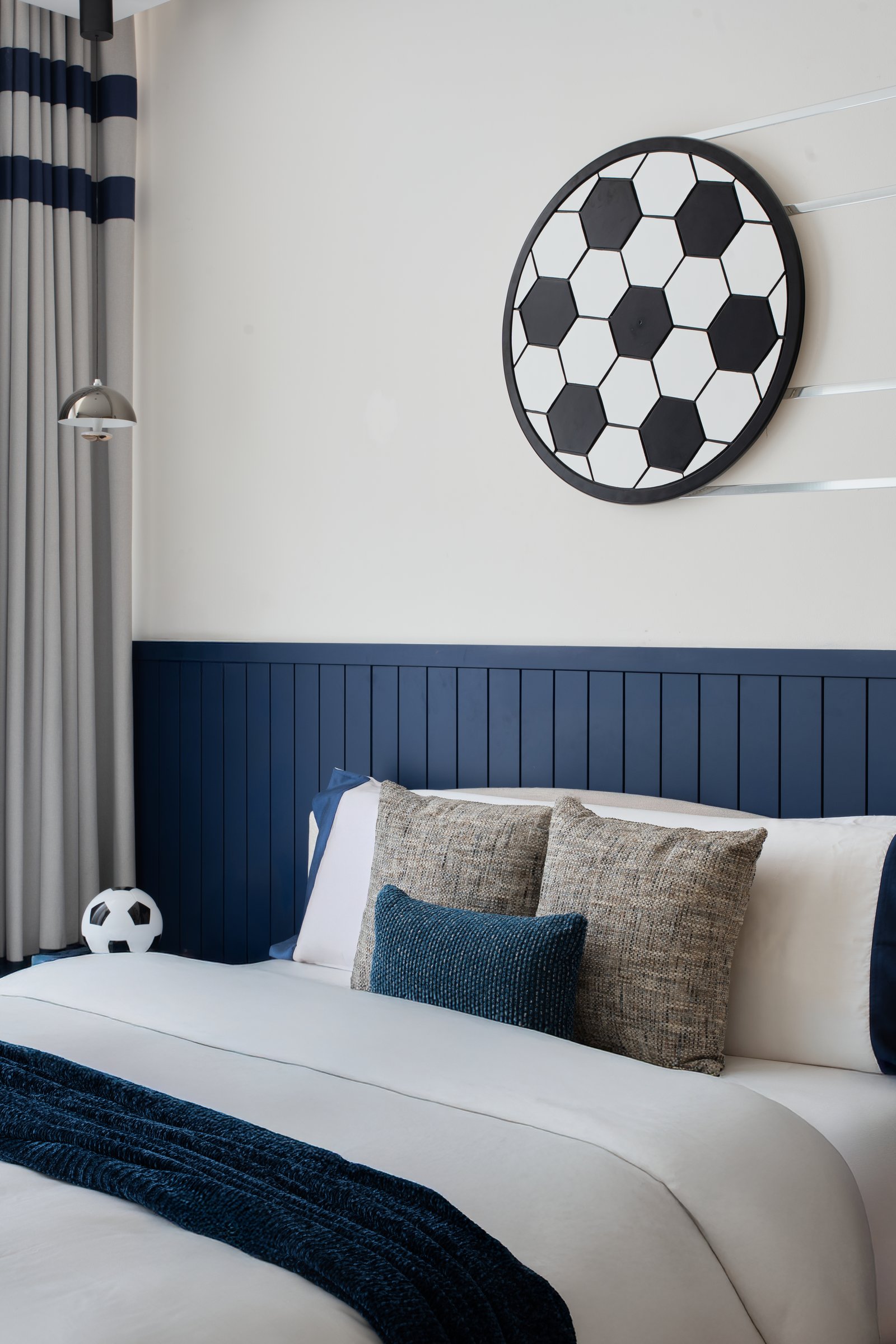 The headboard wall in detail: navy panelling that could belong in a study, kept adult-adjacent by tweed and indigo cushions