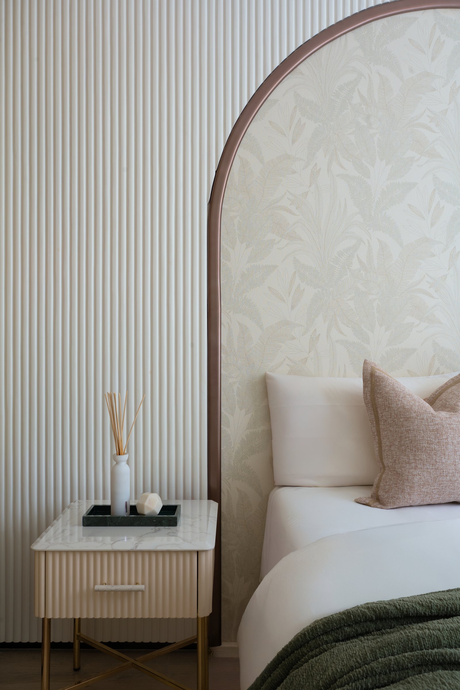 The arched headboard resolving against the fluted wall, with a slim stone-topped bedside cabinet completing the composition