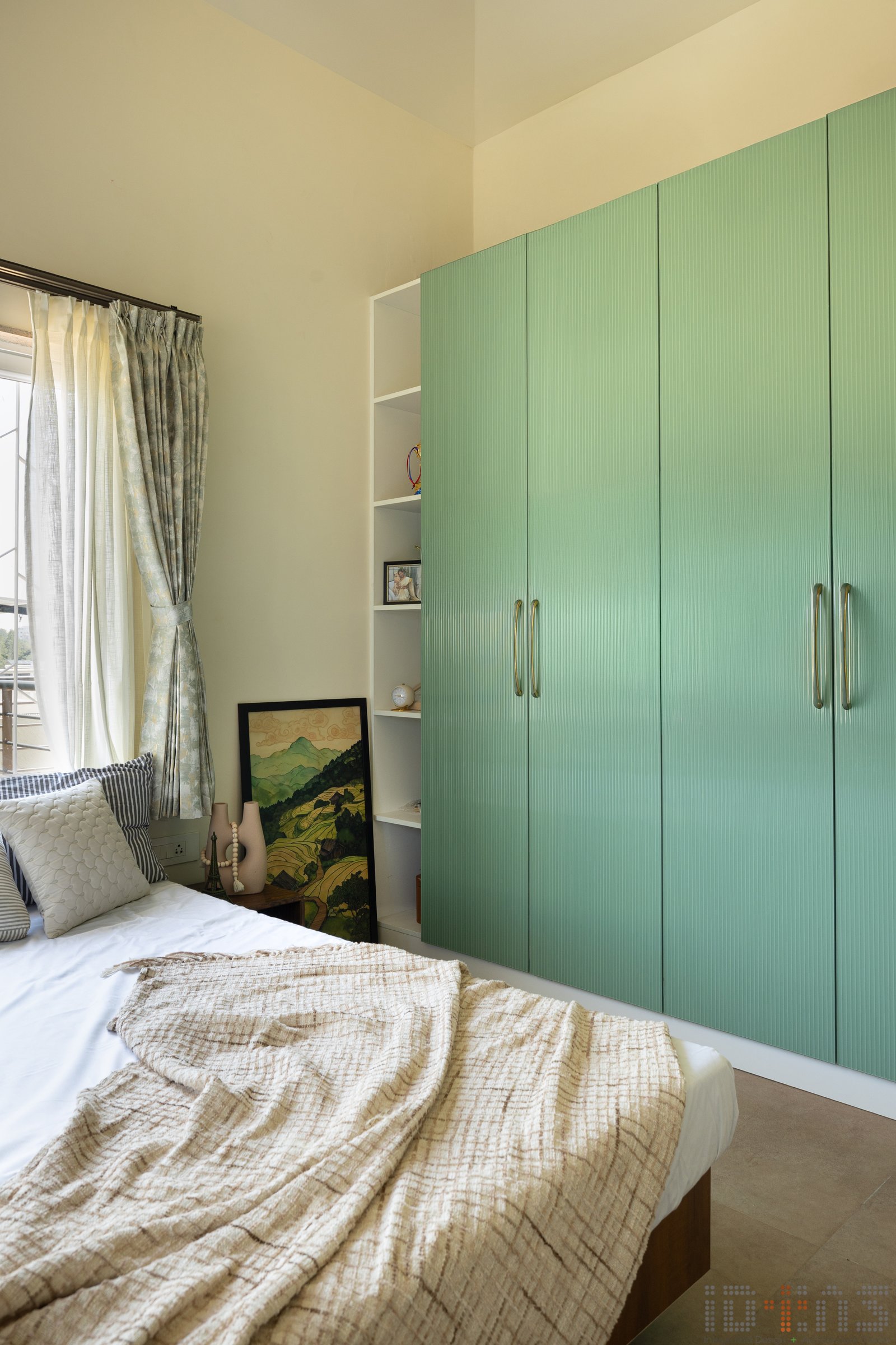 A fluted sage-green wardrobe becomes the room's single declarative gesture, picking up the framed landscape on the open shelf