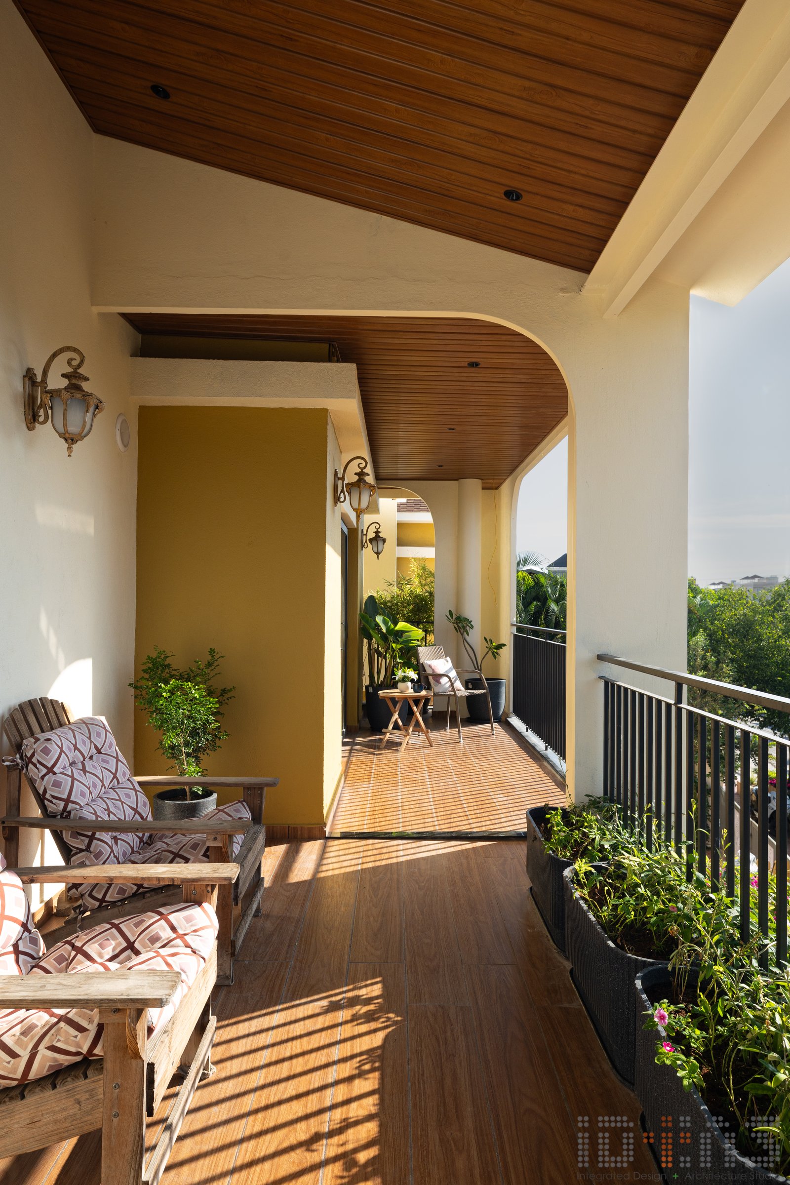 The first-floor balcony, deep and wood-clad above, runs the length of the bedrooms and turns into an outdoor room of its own