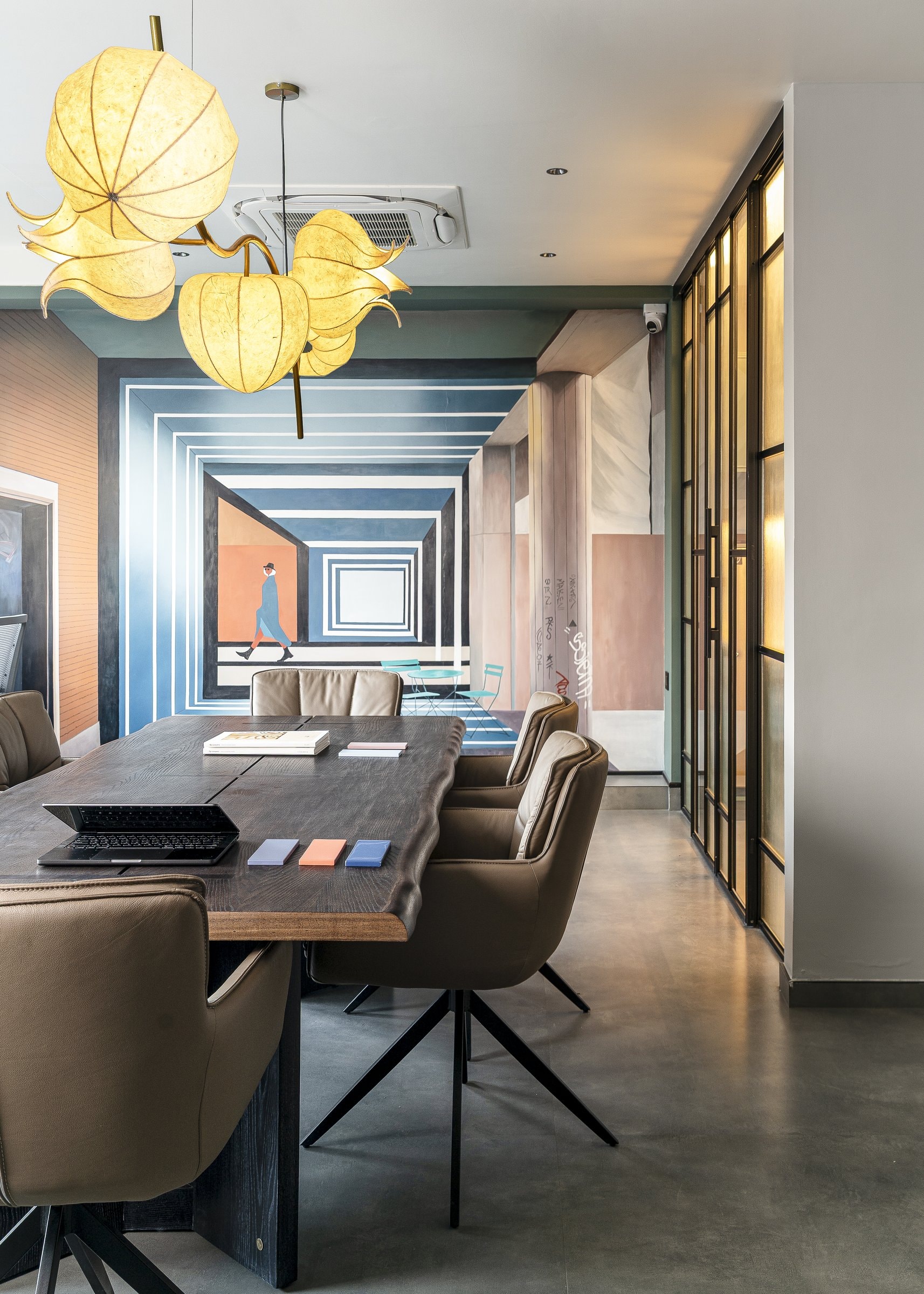 Seen lengthwise, the meeting table, fabric-pod pendant, and fluted glass pantry partition compose the studio's working heart