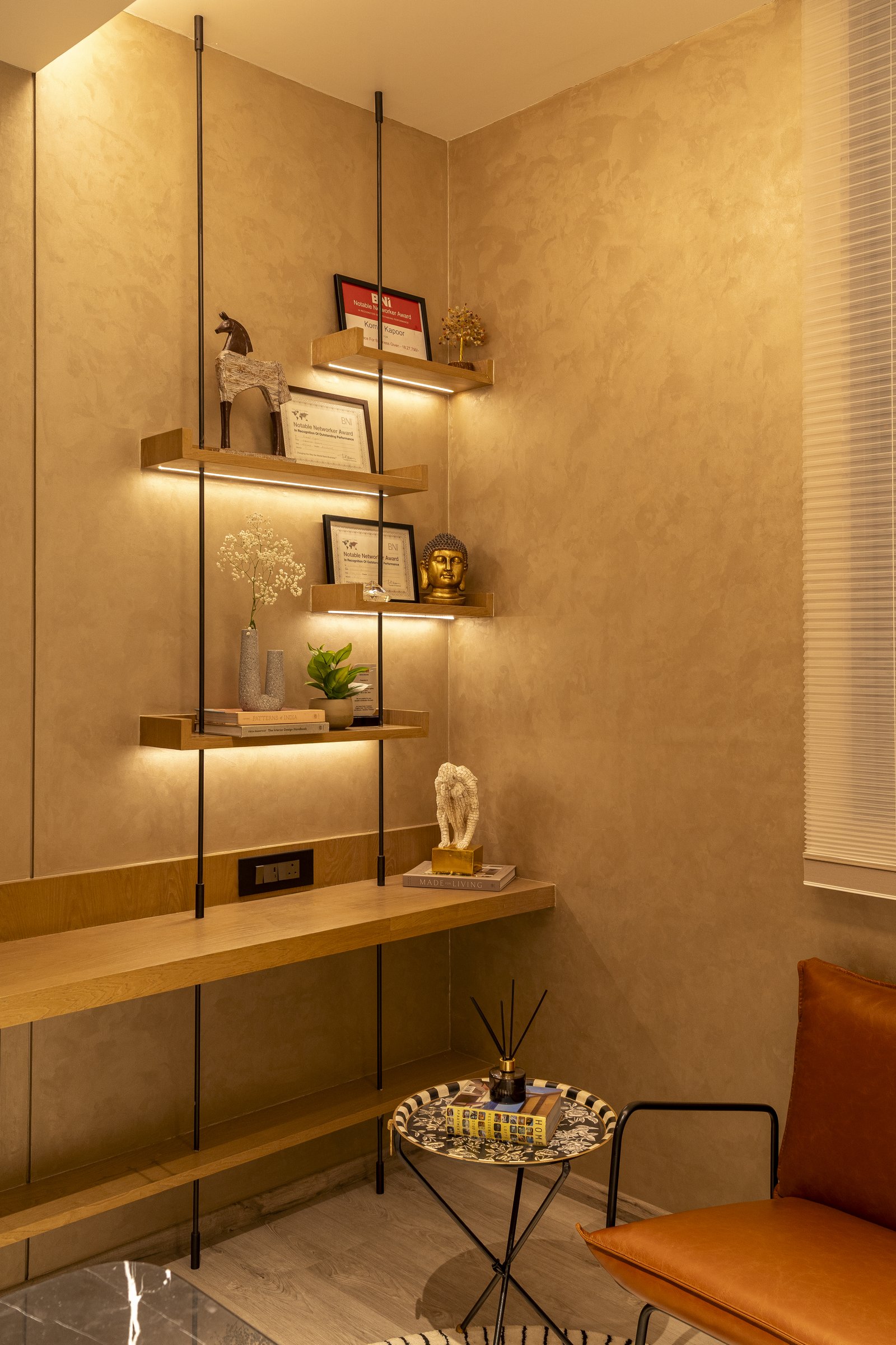 The studio's quiet self-portrait: a suspended shelving rig of wooden ledges lit from below, carrying awards and small objects