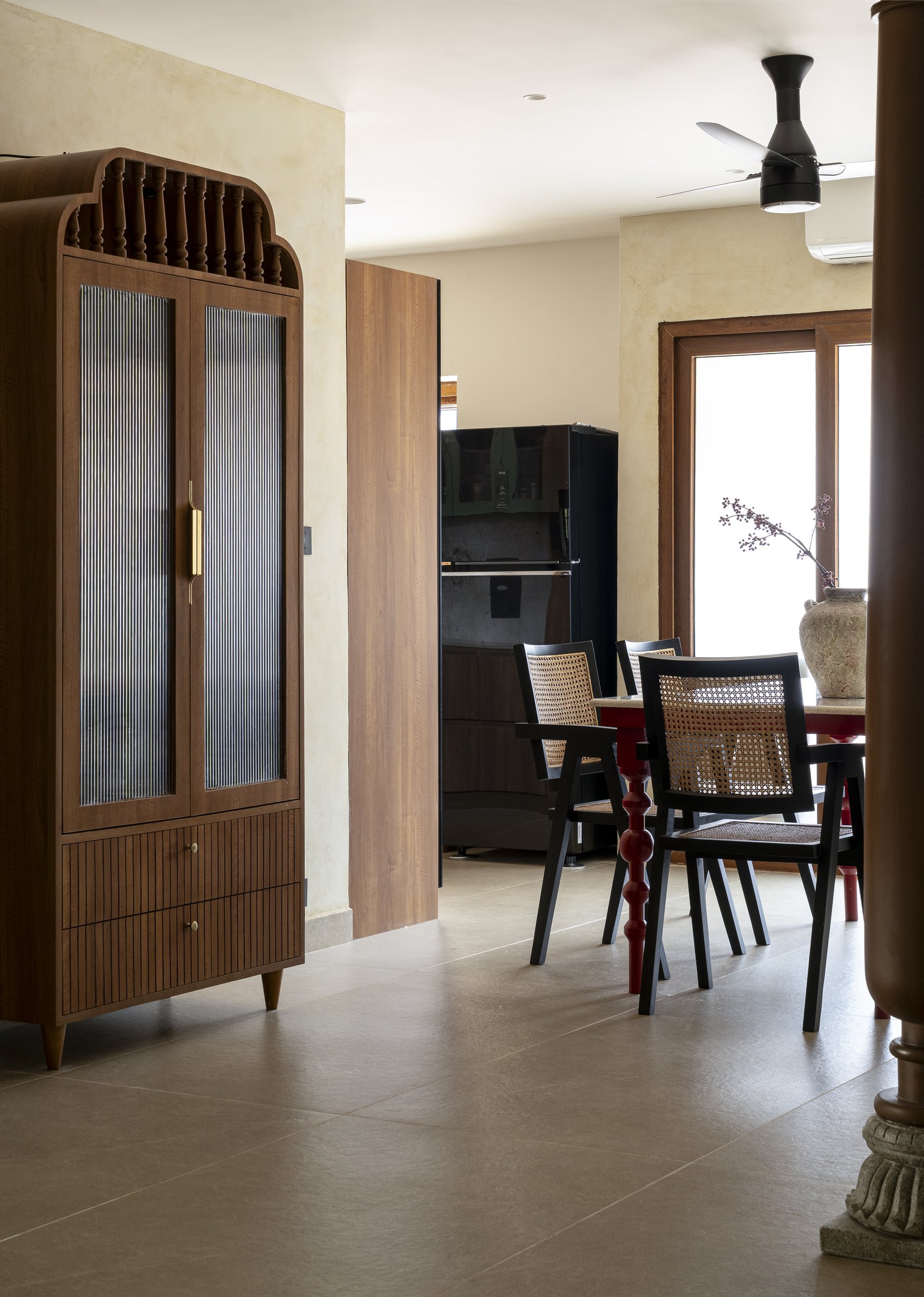 Looking from the pooja cabinet toward the dining and kitchen beyond, the lime-plastered walls carry a single warm tone across the public zones